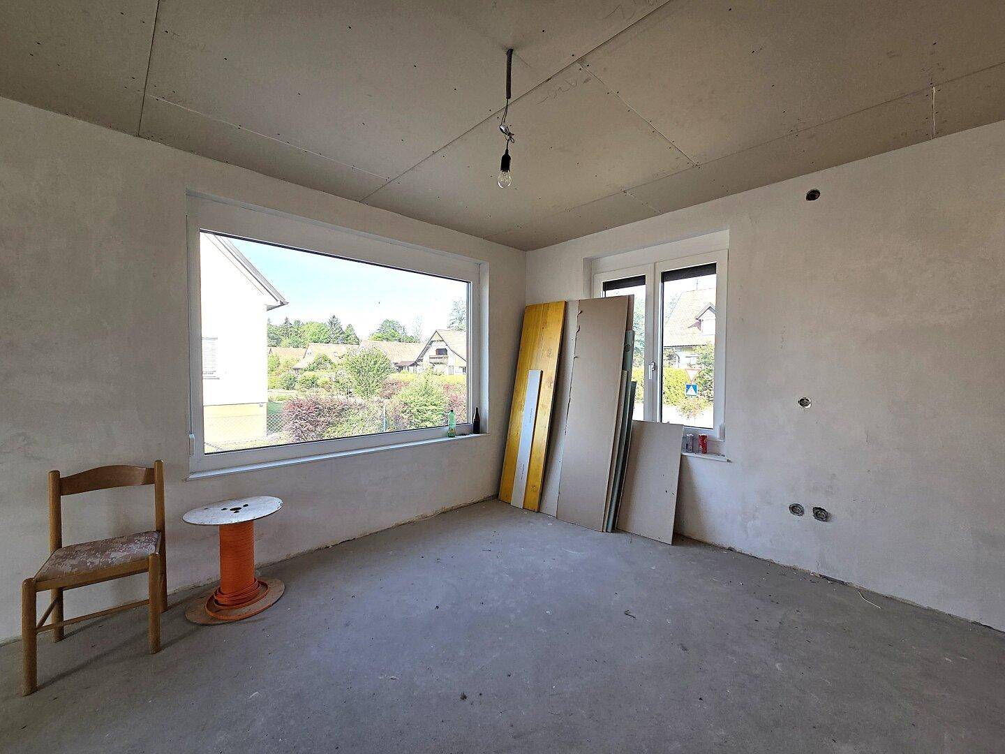 Helles Zimmer im Rohbau mit breitem Fenster und Blick auf die Umgebung.