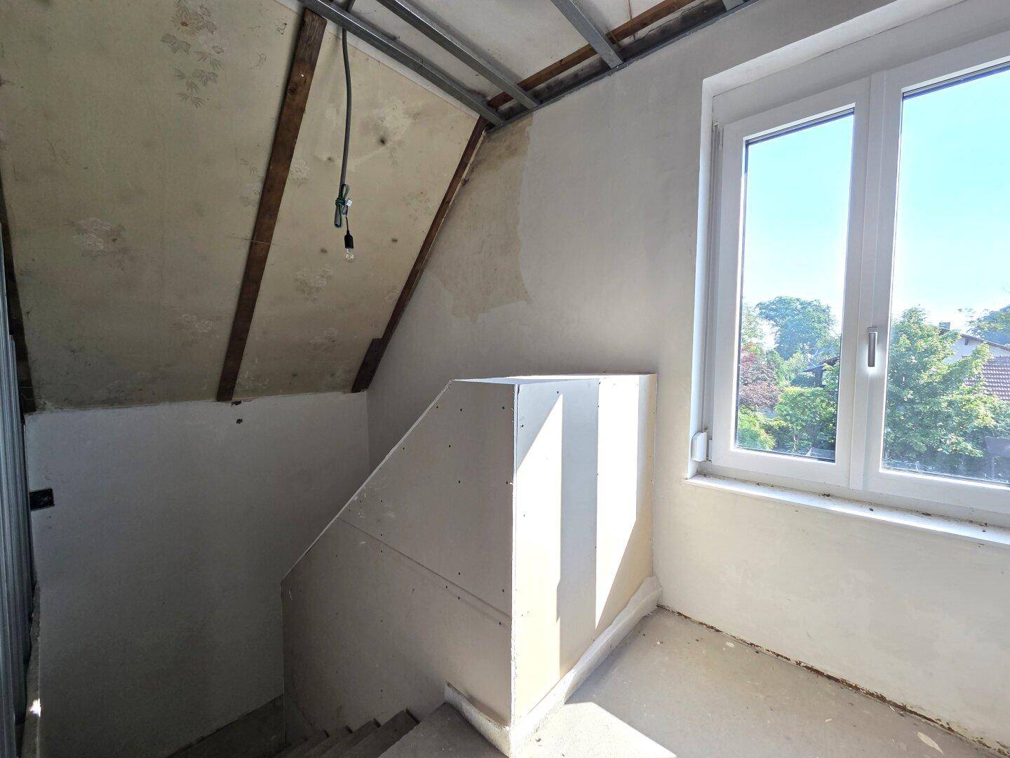 Treppenhaus im Rohbau mit Fenster und vorbereiteten Wänden für den Ausbau.