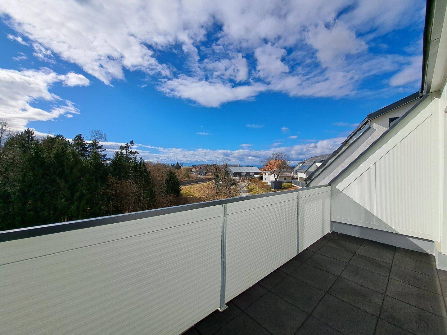 Geräumiger Balkon mit weitem Blick über die Landschaft und die umliegenden Häuser unter blauem Himmel.