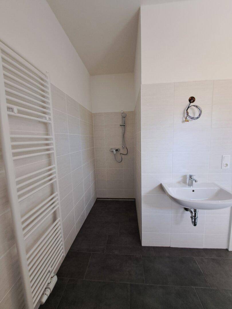 Modernes Badezimmer mit ebenerdiger Dusche, Handtuchheizkörper und hellen Fliesen in neuwertigem Zustand.