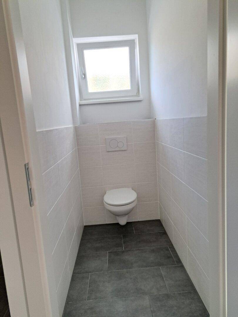 Separates WC mit wandhängender Toilette, Fenster und modernen Fliesen in neuwertigem Zustand.