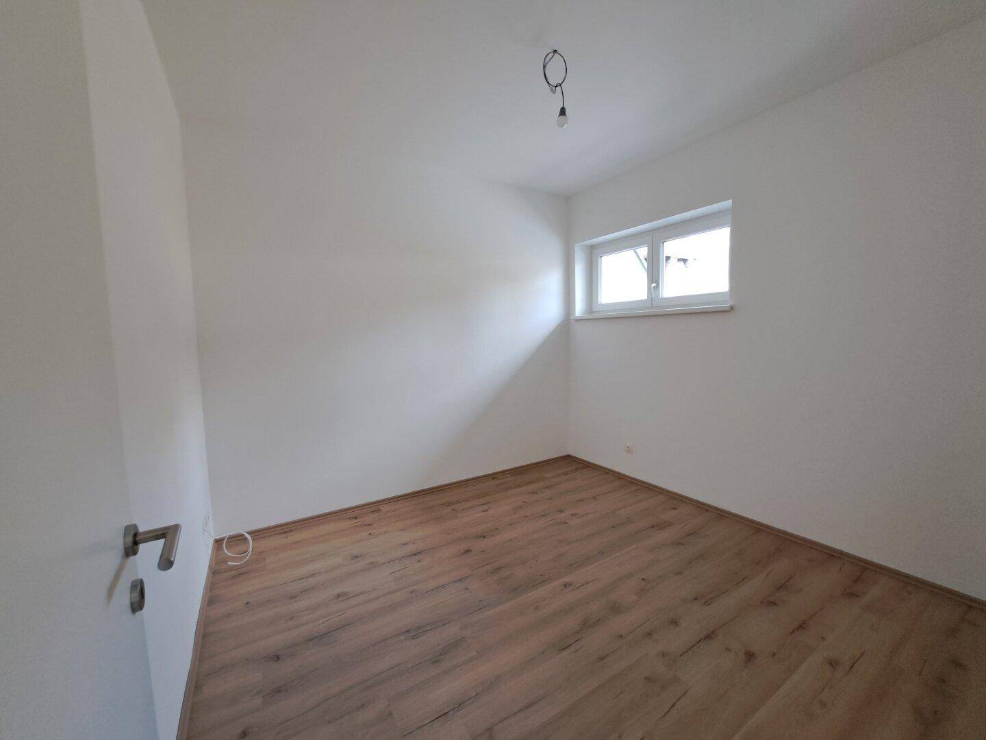 Freundliches Zimmer mit Laminatboden und einem Fenster, ideal als Schlaf- oder Arbeitszimmer.