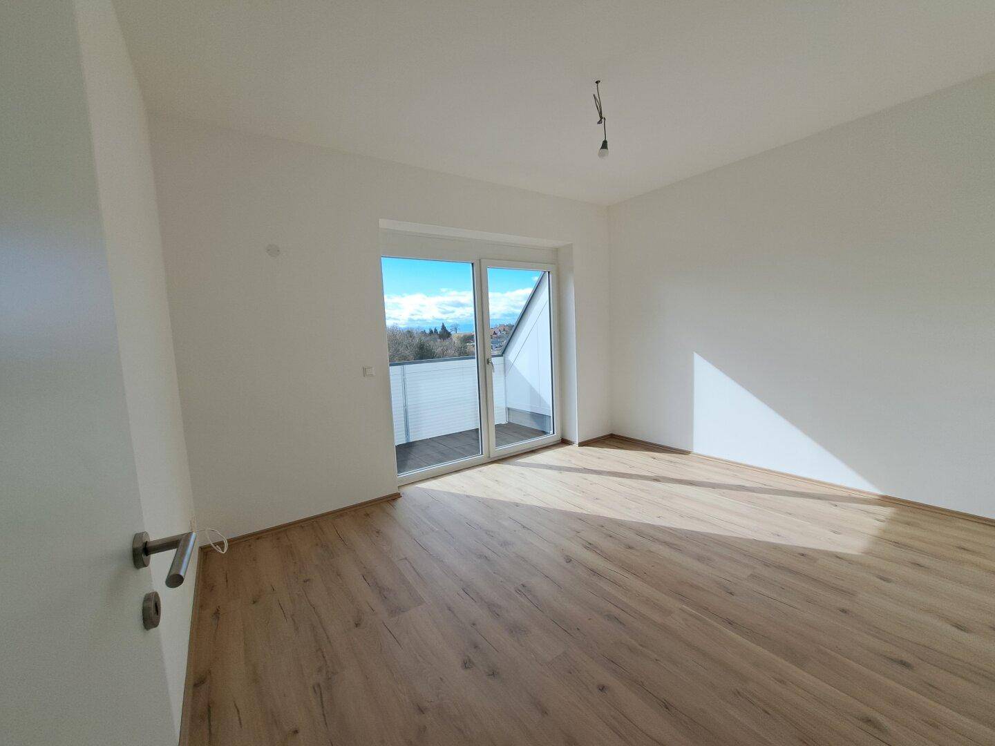 Helles Zimmer mit Laminatboden und Zugang zu einem Balkon, bietet einen weiten Ausblick.
