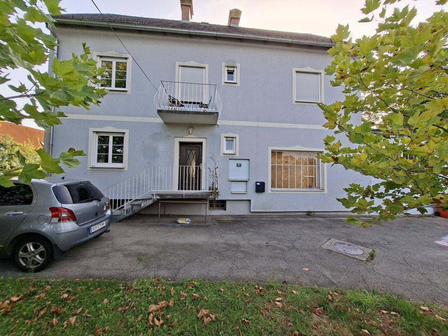 Vorderansicht des Hauses mit hellblauer Fassade, kleinem Balkon über dem Eingang und einem geparkten Auto.