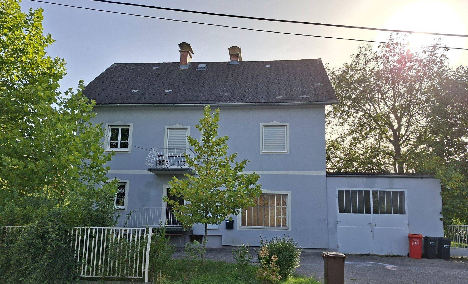 Gesamtansicht der Hausfassade mit kleinem Balkon, angrenzender Garage und einem Baum im Vorgarten.