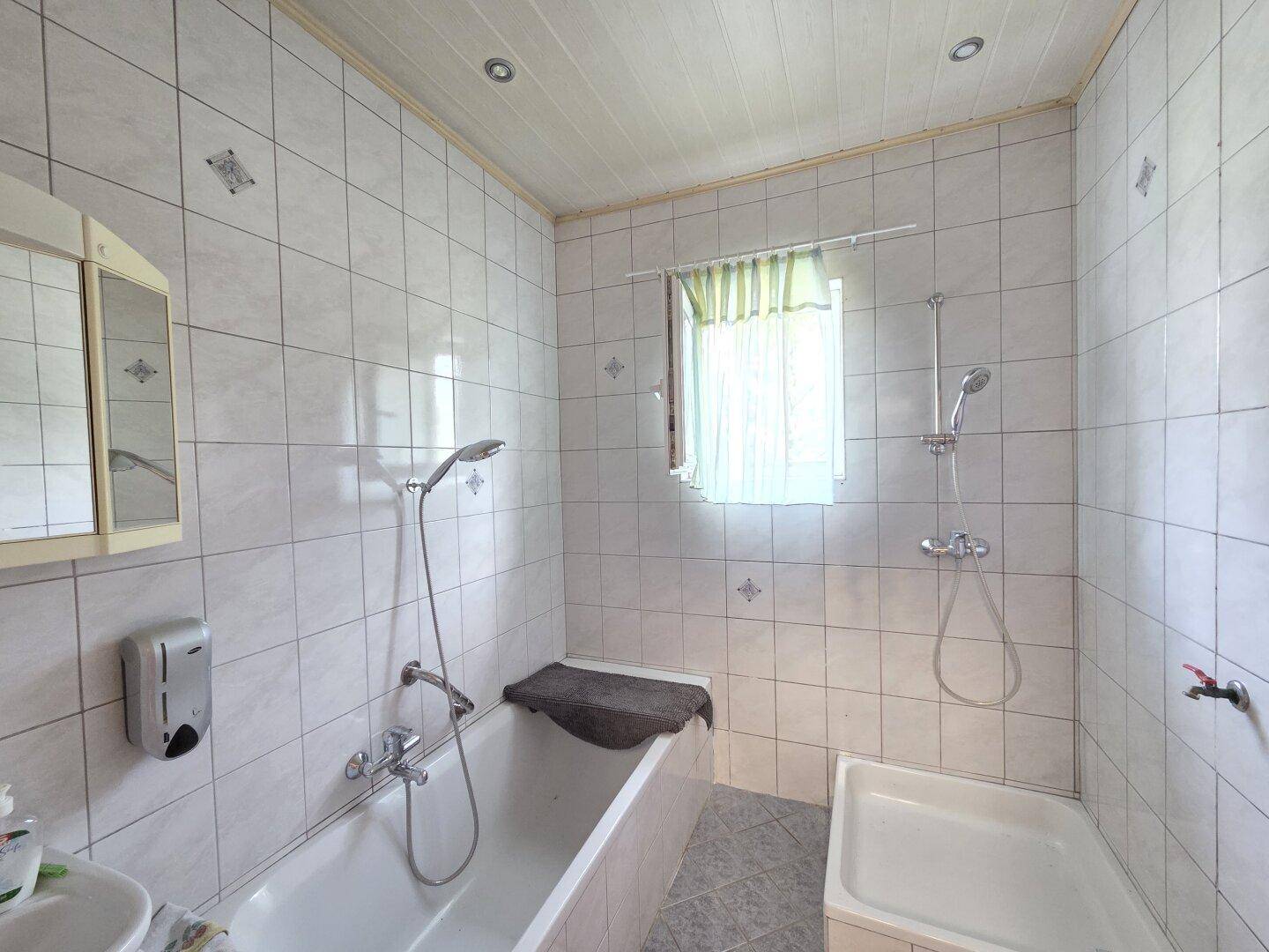 Helles Badezimmer mit Badewanne, Dusche und weißen Fliesen.
