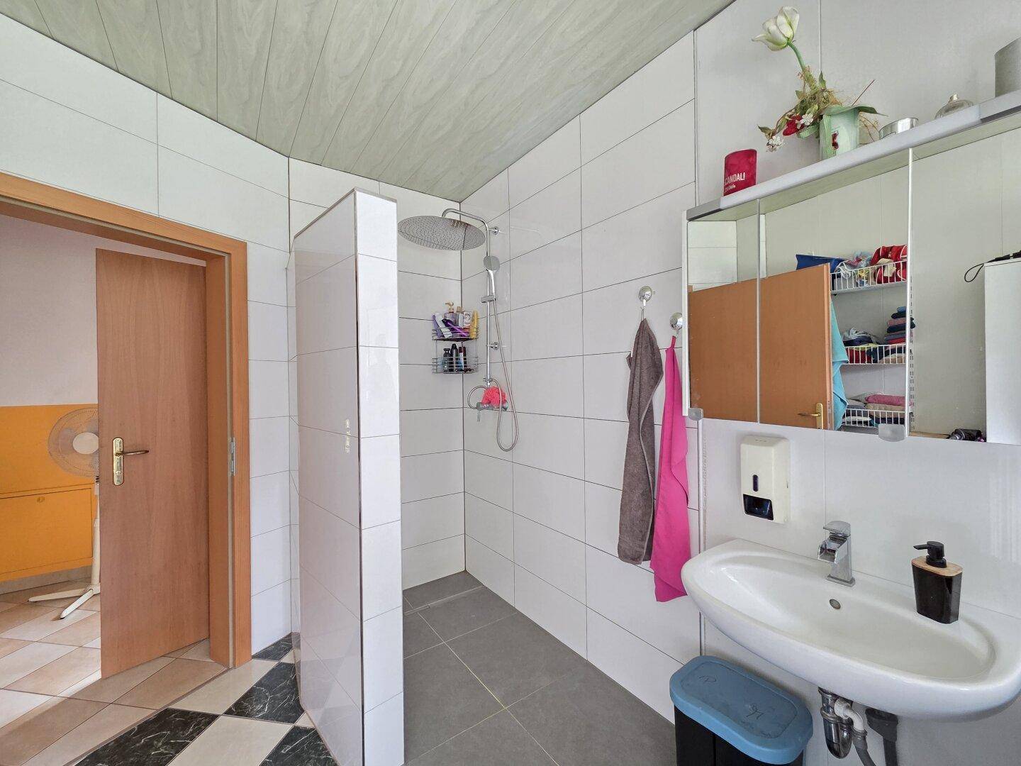 Modernisiertes Badezimmer mit ebenerdiger Dusche, Waschbecken und Spiegel.