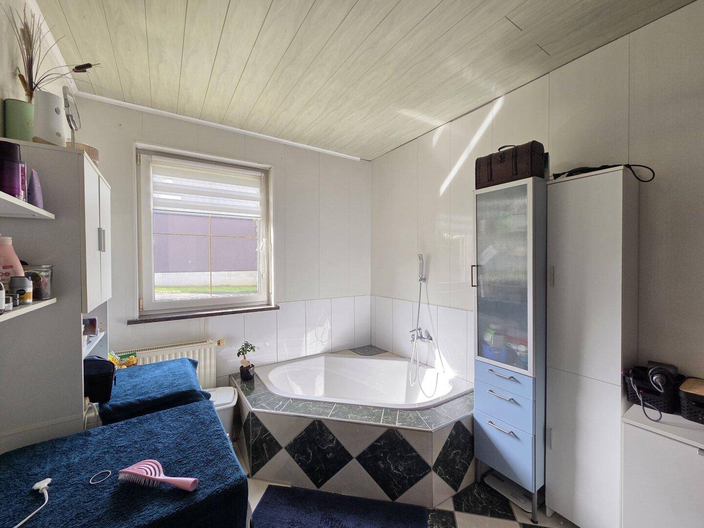 Badezimmer mit Eckbadewanne, Fenster und Stauraum.