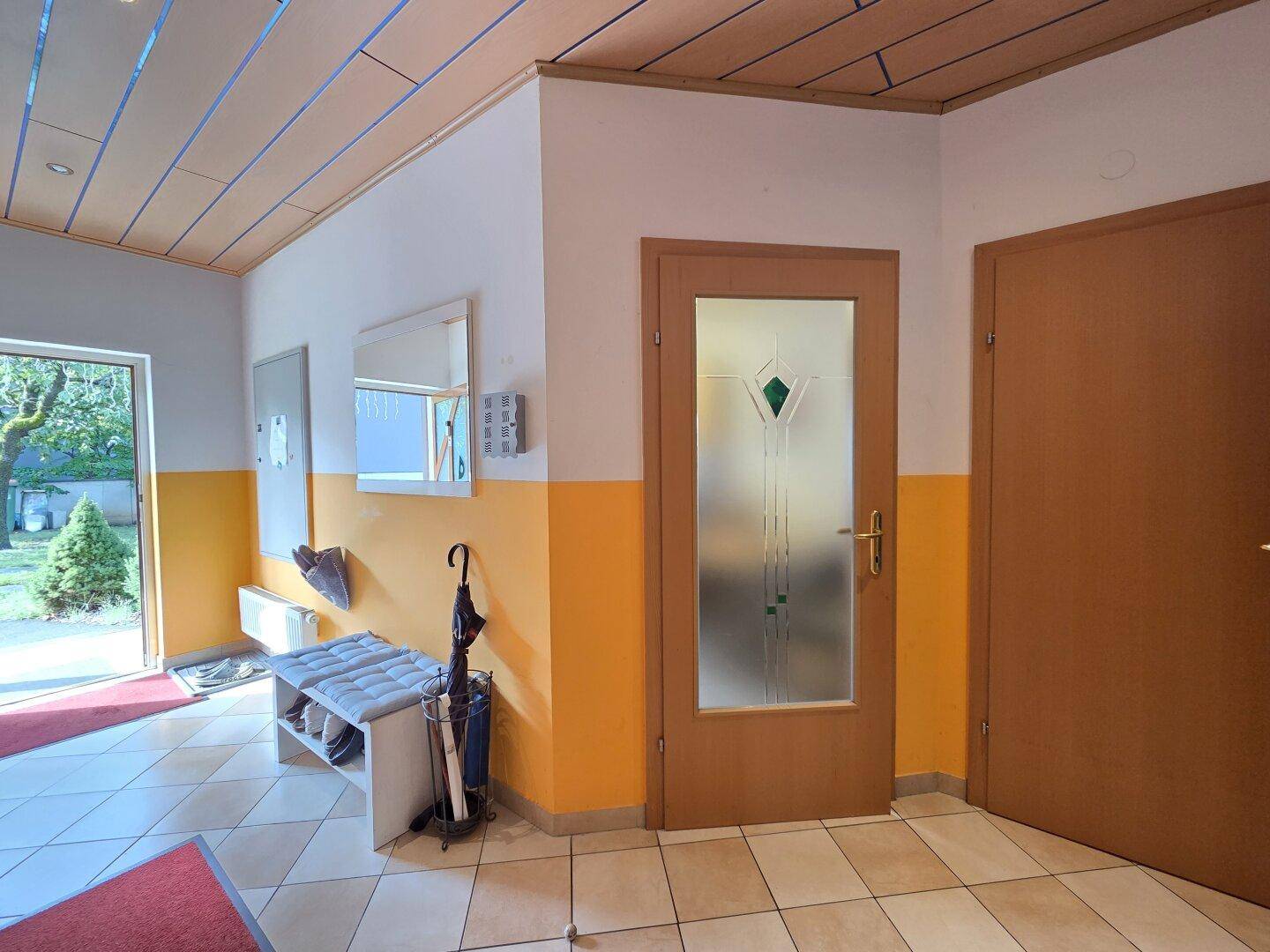 Heller Eingangsbereich mit Fliesenboden, Holzdecke und Garderobe.