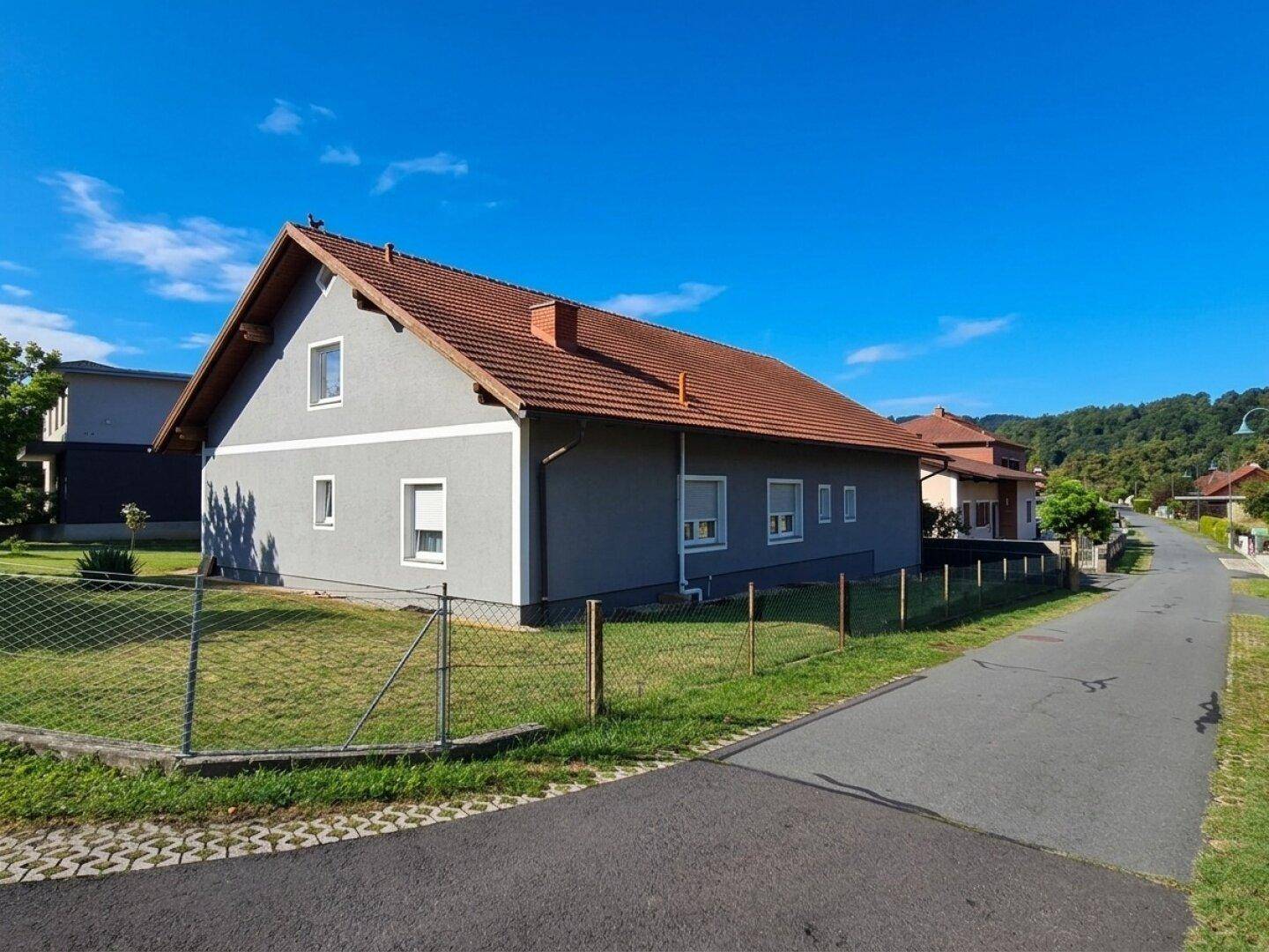 Seitenansicht des Hauses mit Zaun und angrenzender Straße in ländlicher Umgebung.