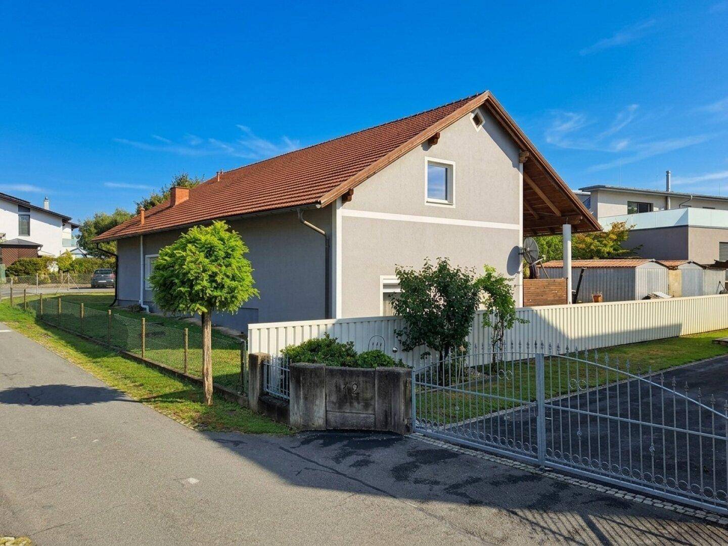 Ansicht des Hauses von der Straße mit Einfahrtstor und kleinem Baum im Vorgarten.