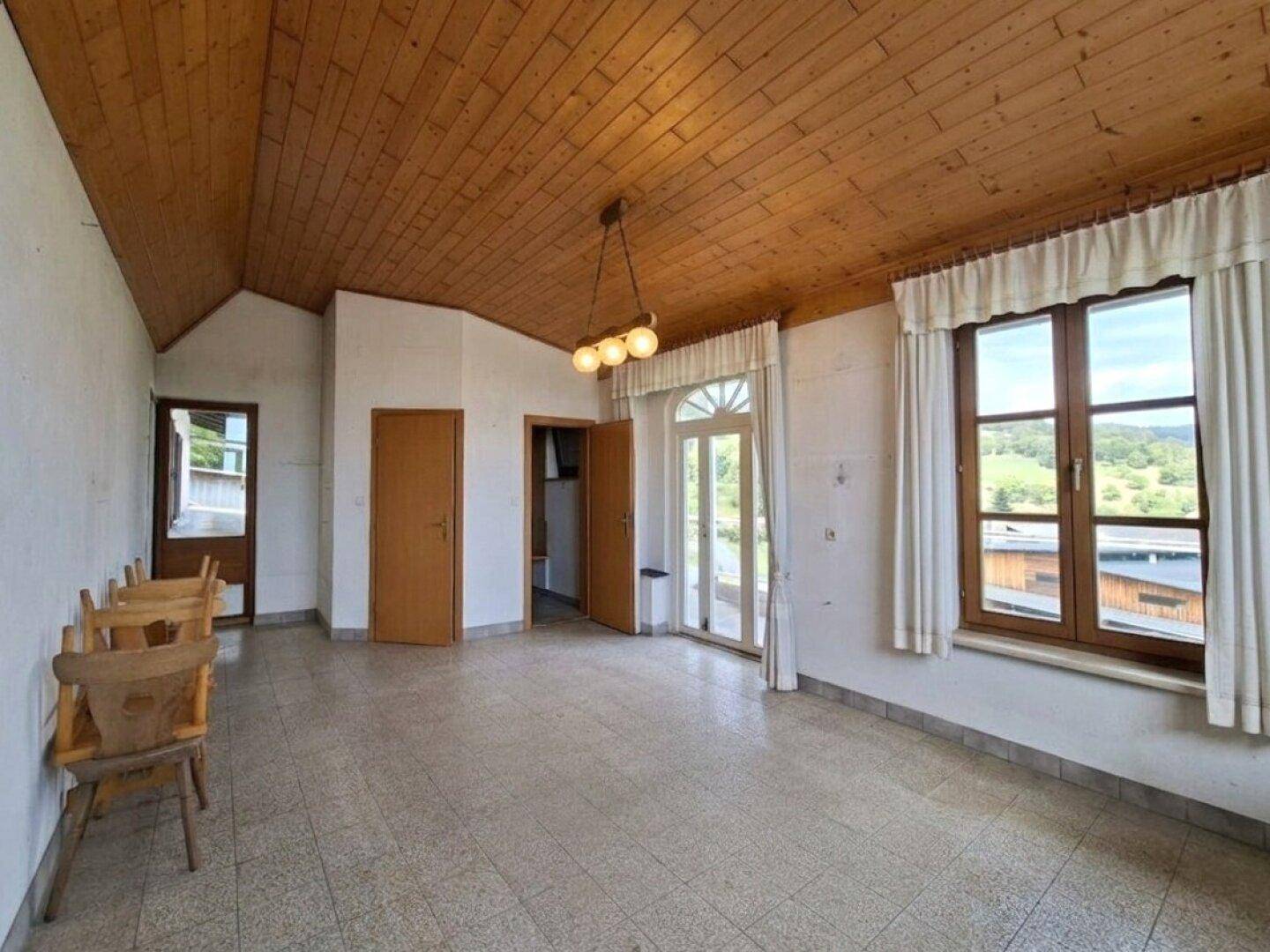 Geräumiger Essbereich mit Holzbalkendecke, Fliesenboden und Blick auf die grüne Landschaft.