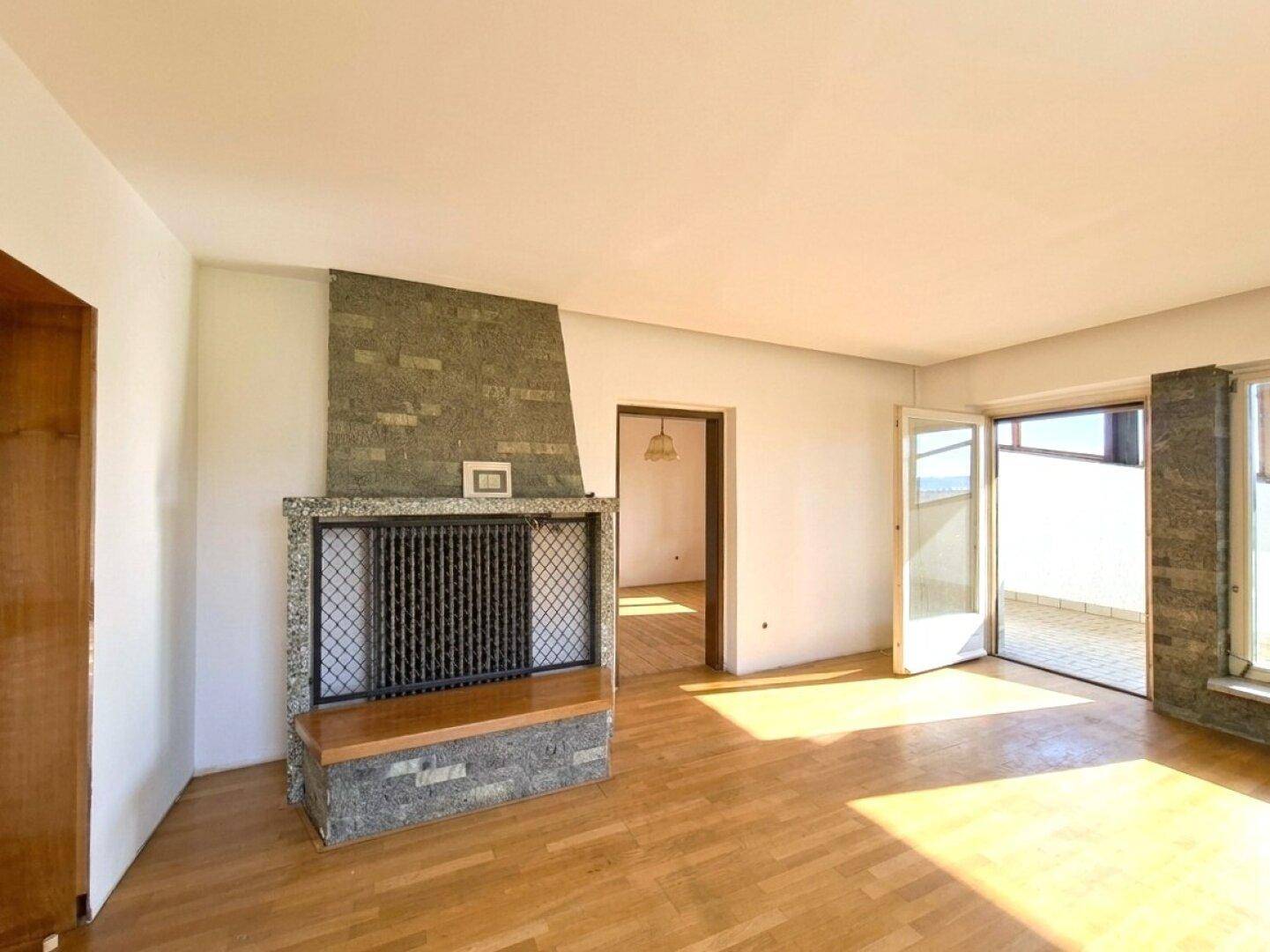 Helles Wohnzimmer mit Kamin aus Naturstein, Parkettboden und Zugang zu einem Balkon.