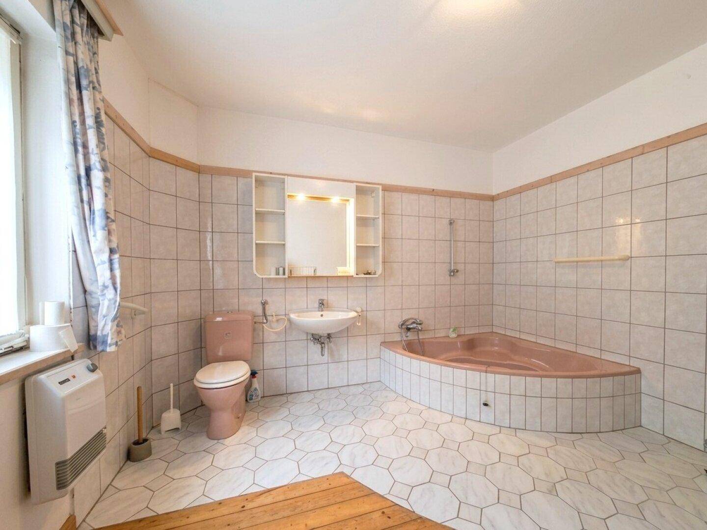 Badezimmer im Stil der 80er Jahre mit rosa Sanitärobjekten, Eckbadewanne und Fliesenboden.