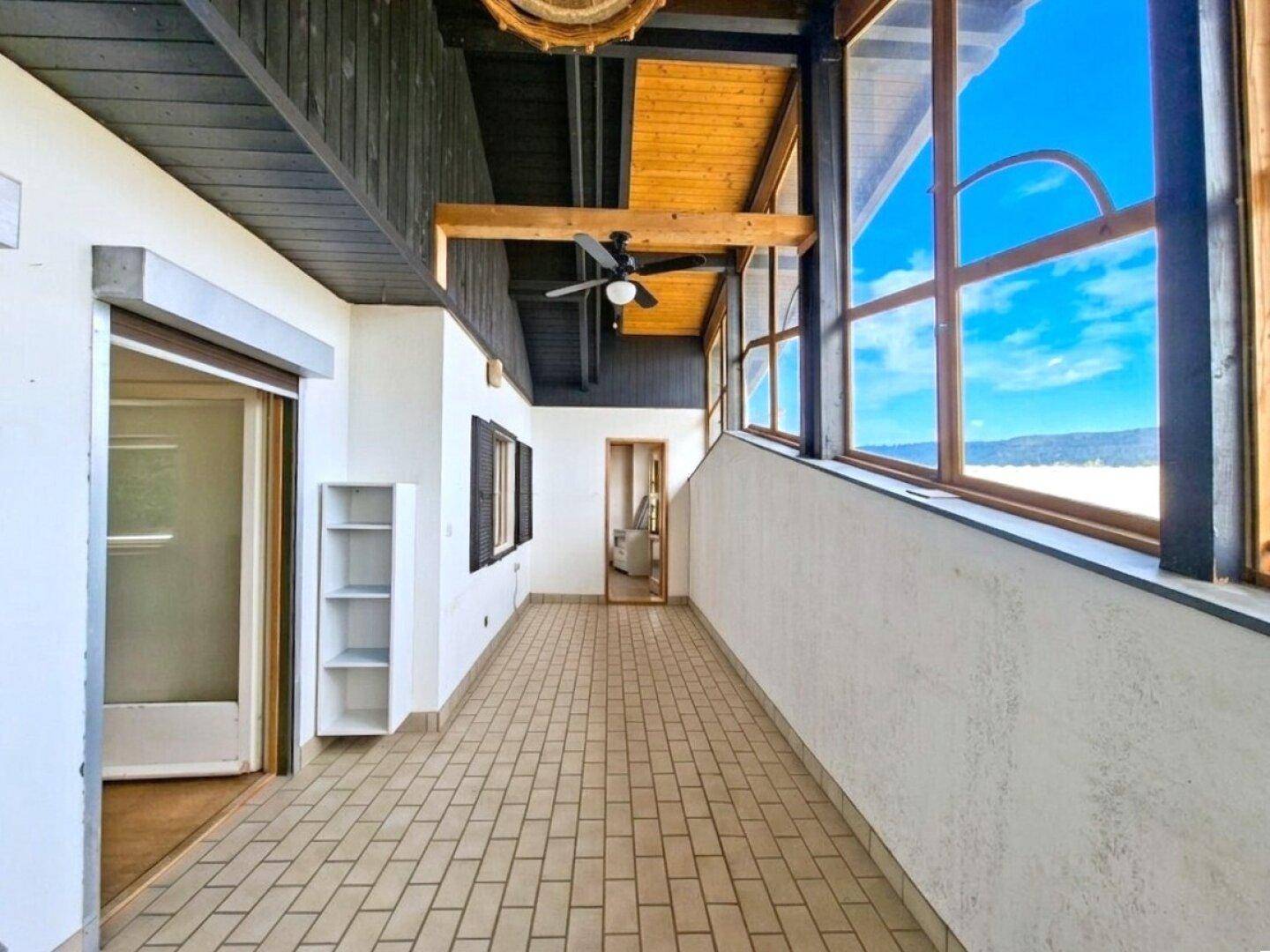 Heller Wintergarten mit großen Fenstern, Fliesenboden und Deckenventilator, ideal zum Entspannen.