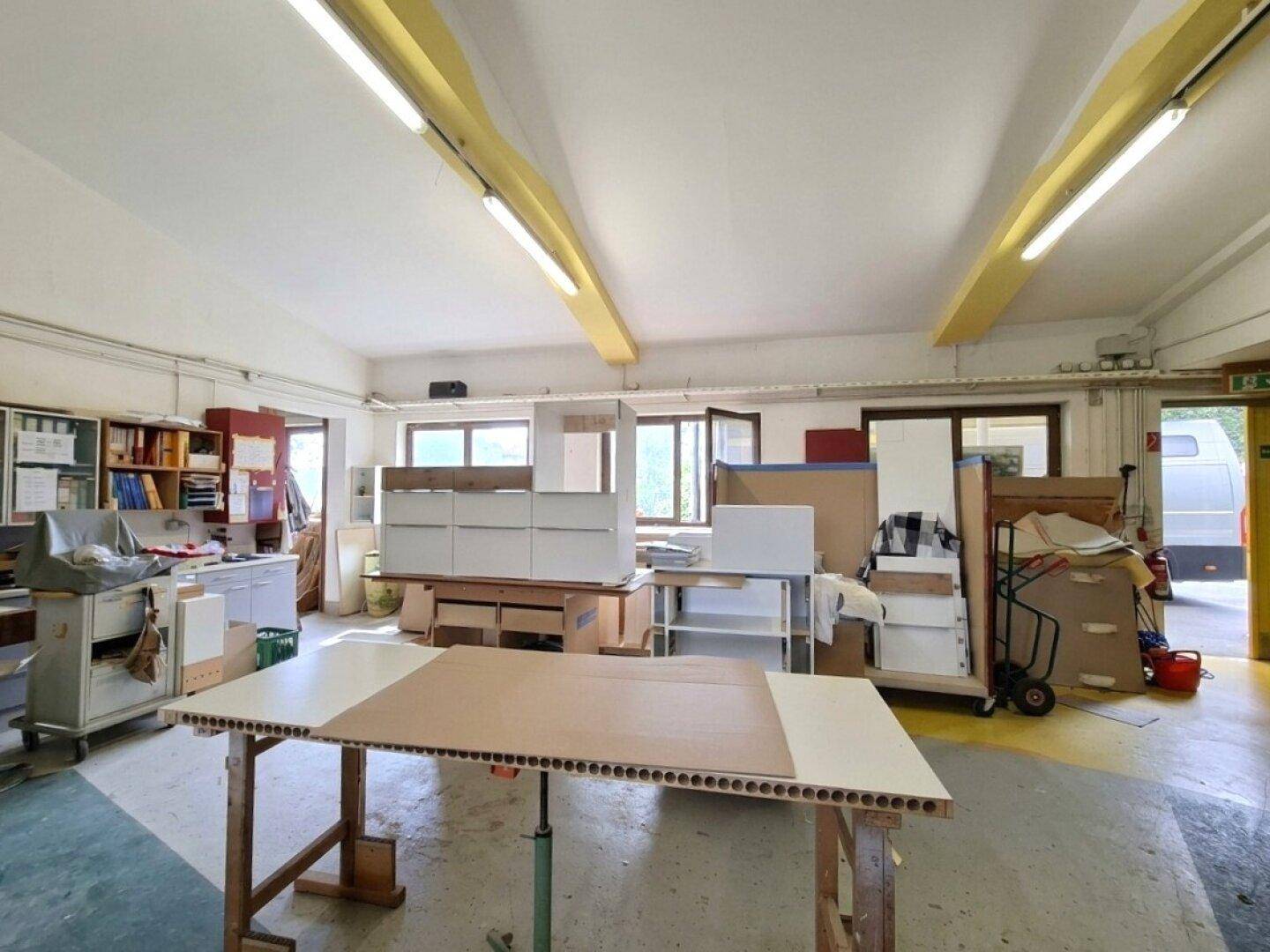 Geräumige Werkstatt mit Arbeitstischen, Lagerflächen und natürlichem Lichteinfall durch Fenster.
