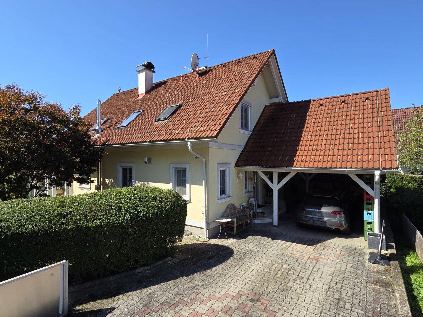 Ansicht des Einfamilienhauses mit Carport und gepflasterter Auffahrt unter blauem Himmel.