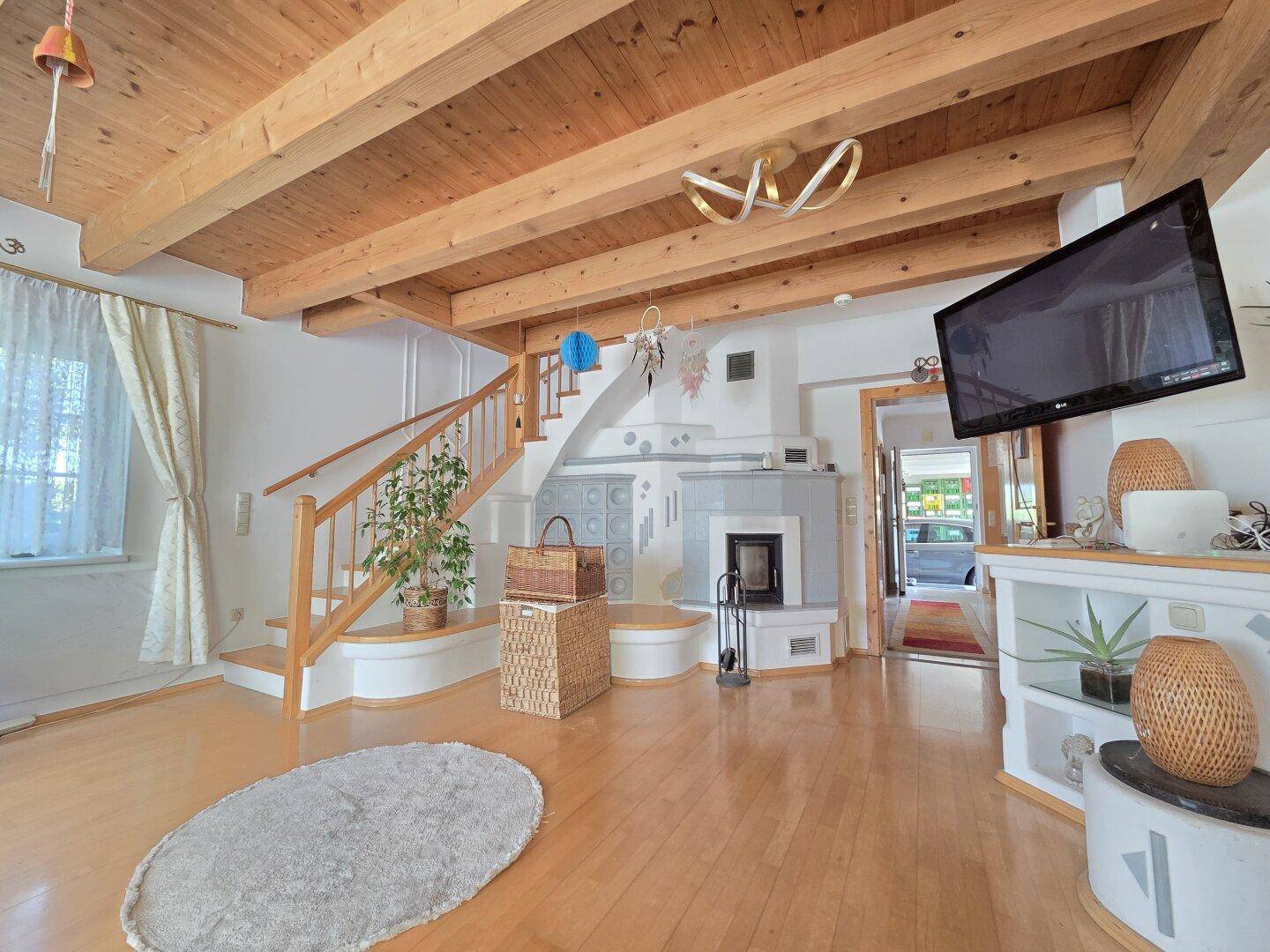Helles Wohnzimmer mit Holzbalkendecke, Parkettboden und traditionellem Kachelofen.