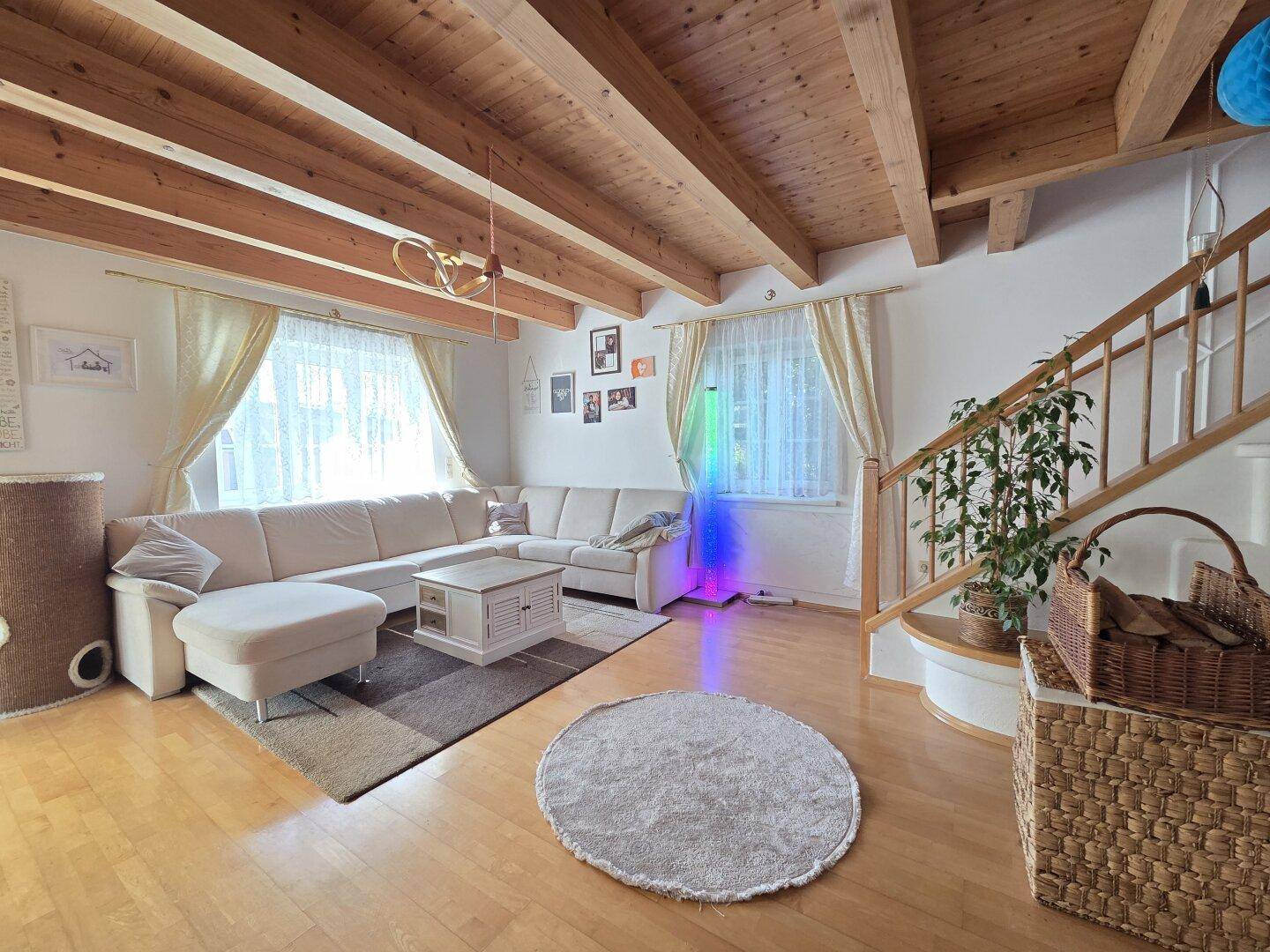 Gemütliches Wohnzimmer mit großem Ecksofa, Holzbalkendecke und Parkettboden.