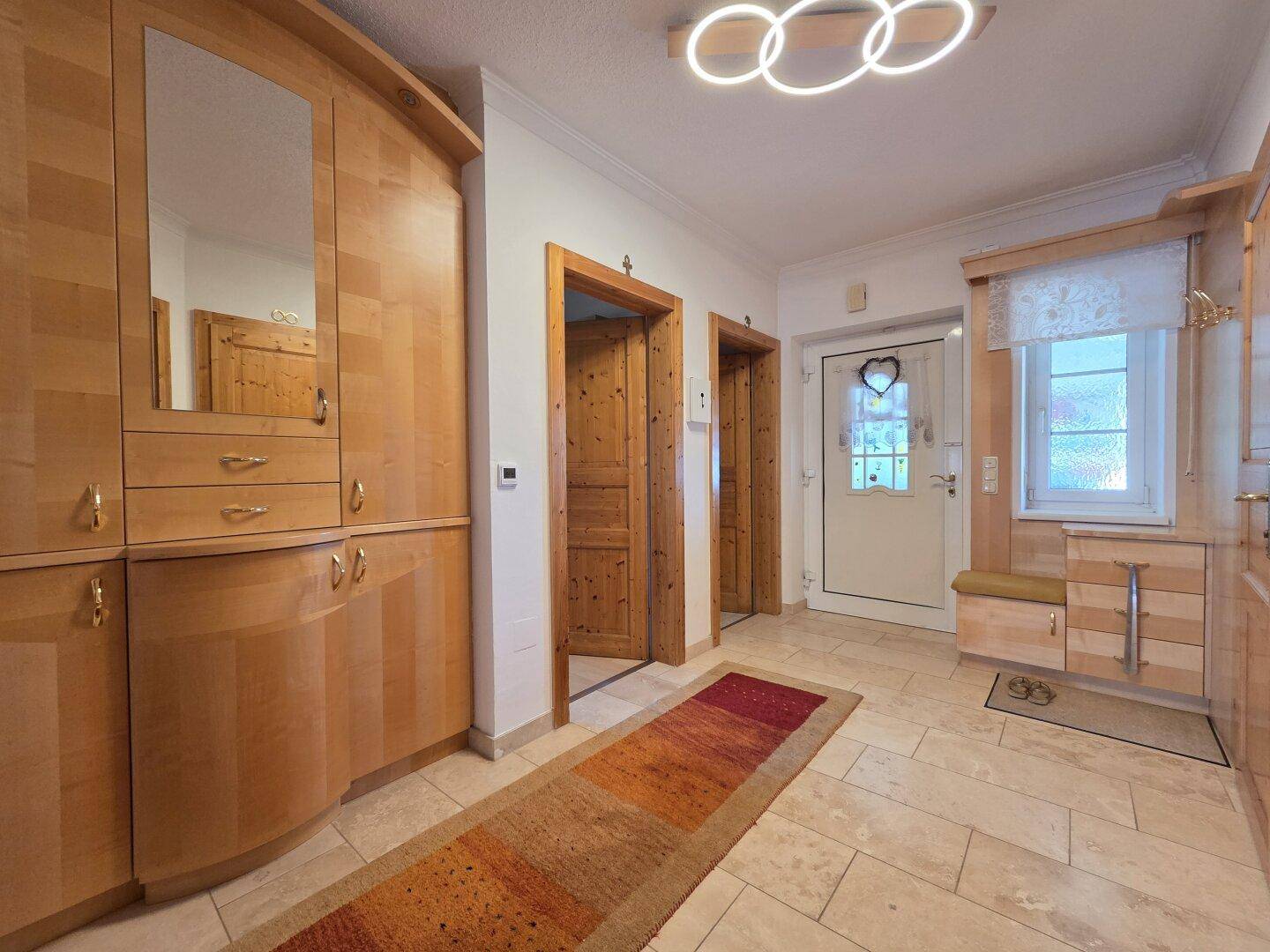 Heller Eingangsbereich mit Einbauschränken aus Holz, Fliesenboden und Garderobe.