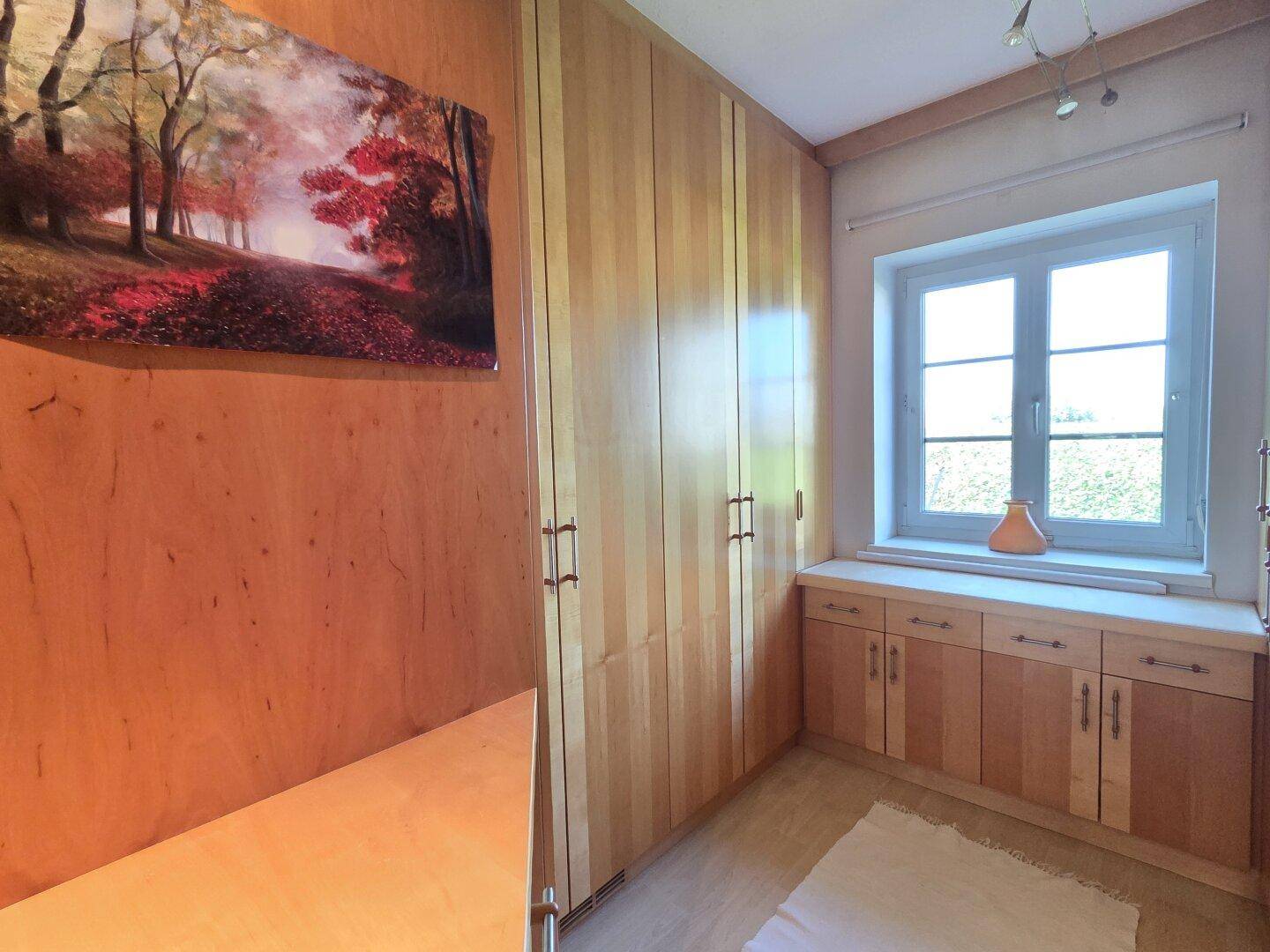 Raum mit Einbauschränken aus hellem Holz und Fenster, ideal als Ankleidezimmer.