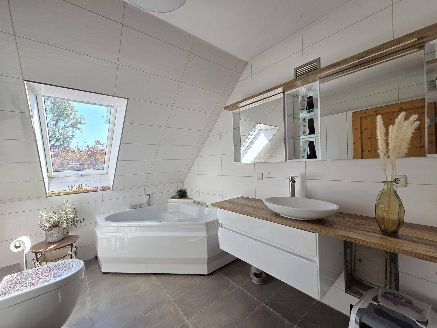 Großes Badezimmer im Dachgeschoss mit Eckbadewanne, Dachfenster und modernem Waschtisch.