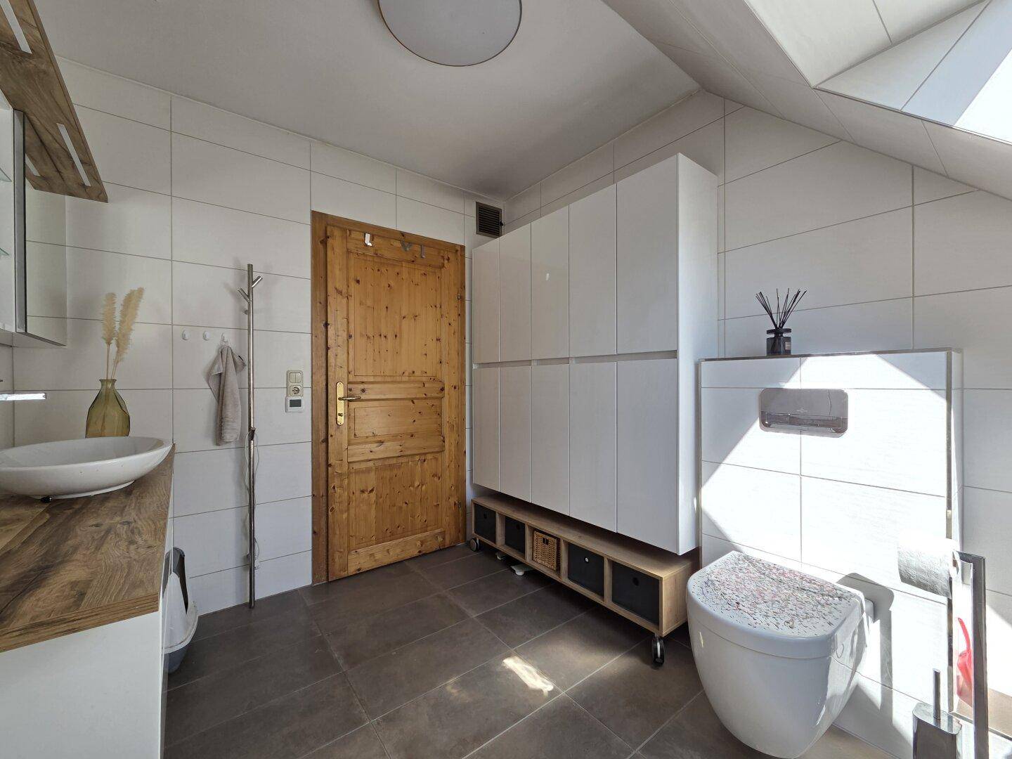 Badezimmer mit Fliesenboden, Wand-WC und Einbauschränken unter der Dachschräge.