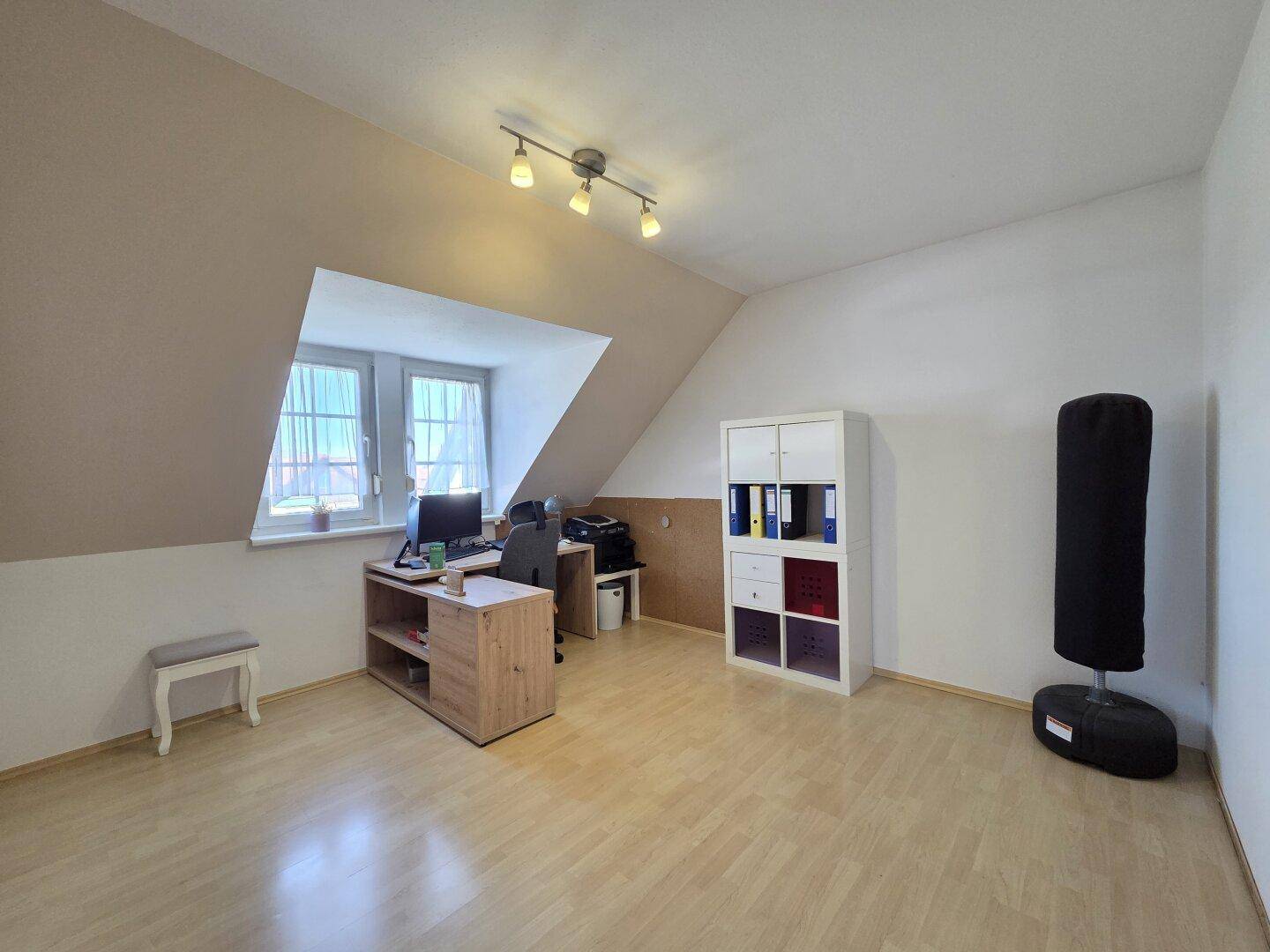 Geräumiges Büro im Dachgeschoss mit Schreibtisch, Regalen und Dachschräge.