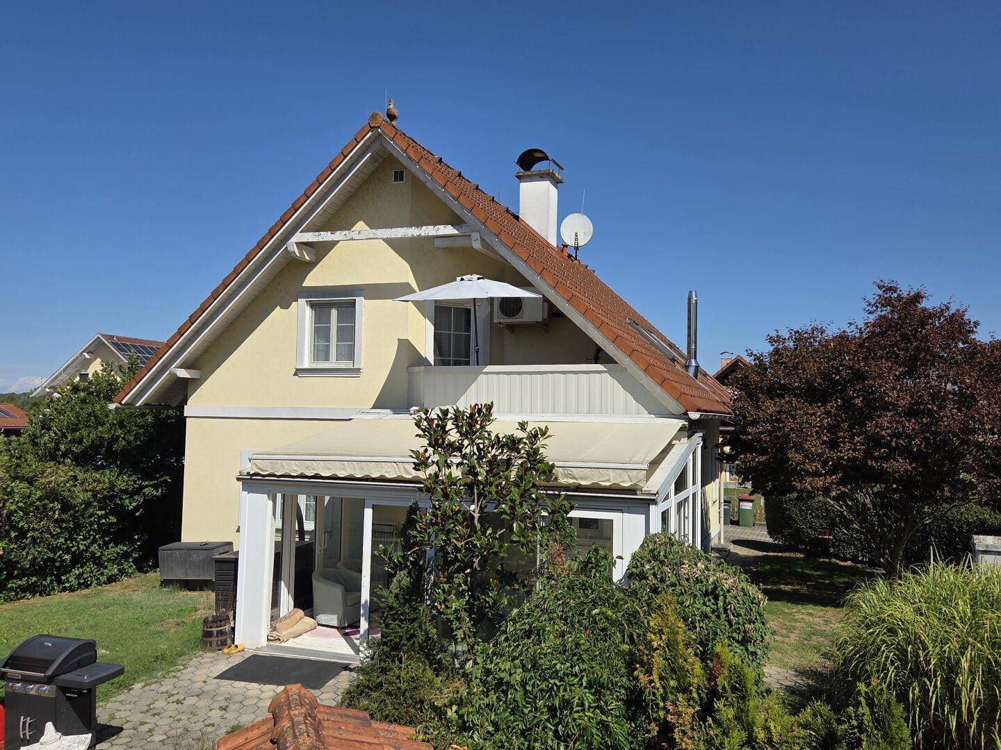 Rückansicht des Hauses mit Balkon, Wintergarten und Grillplatz im Garten.