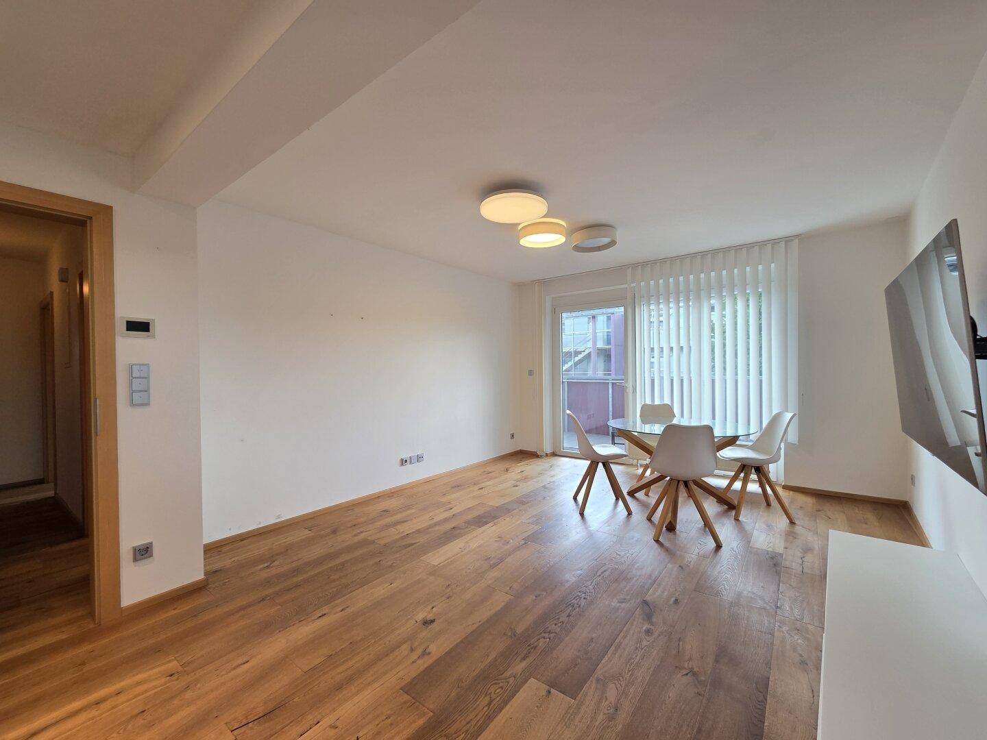 Geräumiger Wohnbereich mit Holzboden, Esstisch und Zugang zum Balkon.