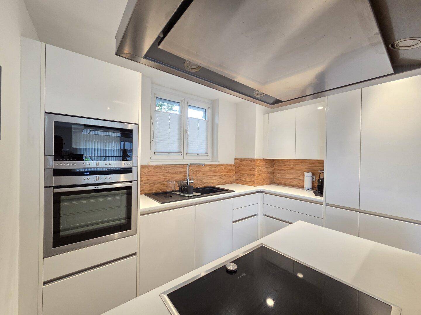Moderne Einbauküche mit weißen Hochglanzfronten, Induktionskochfeld und integriertem Backofen.