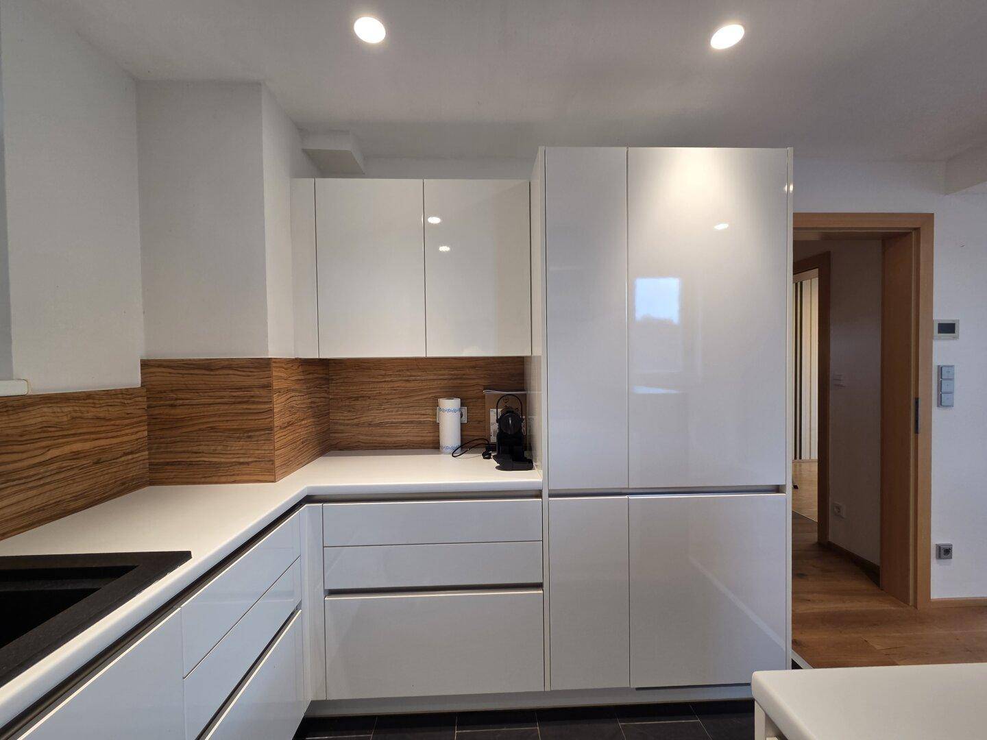 Helle Küche mit weißen Hochglanzschränken, Holzrückwand und integriertem Kühlschrank.