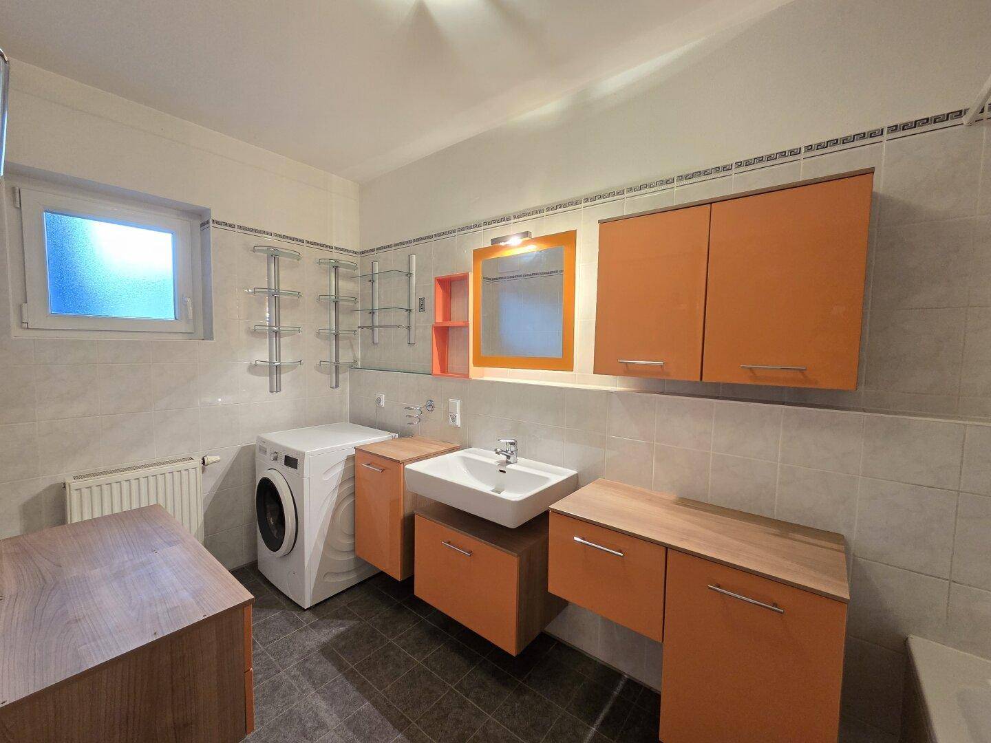 Badezimmer mit Waschmaschine, Einzelwaschbecken und orangefarbenen Schränken.