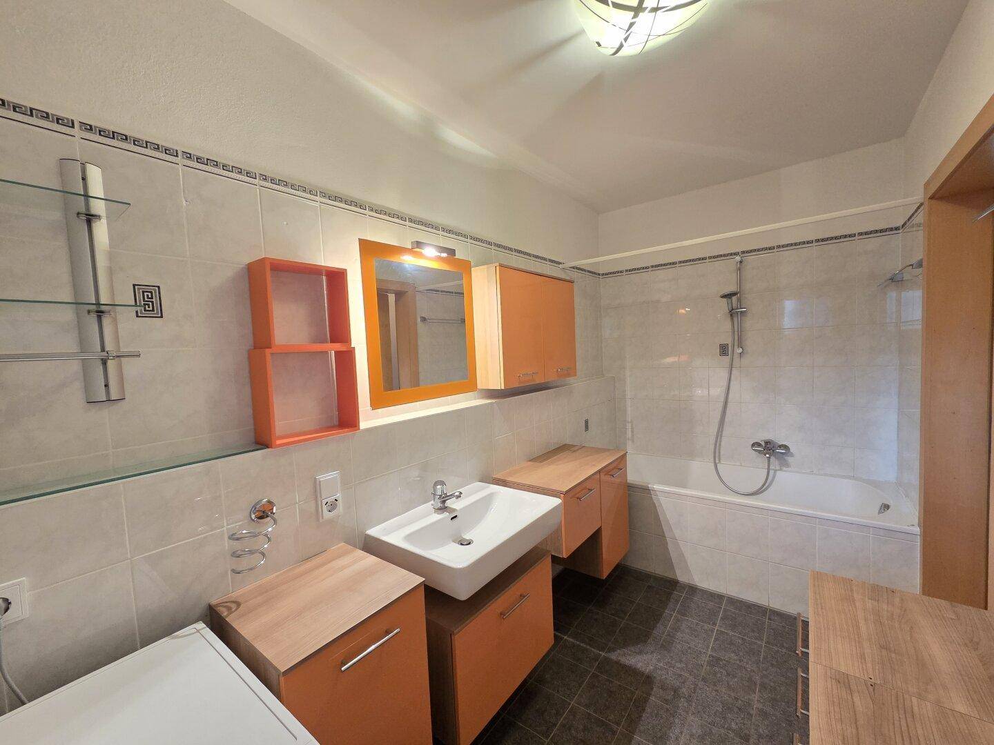Badezimmer mit Badewanne, Einzelwaschbecken und orangefarbenen Badmöbeln.