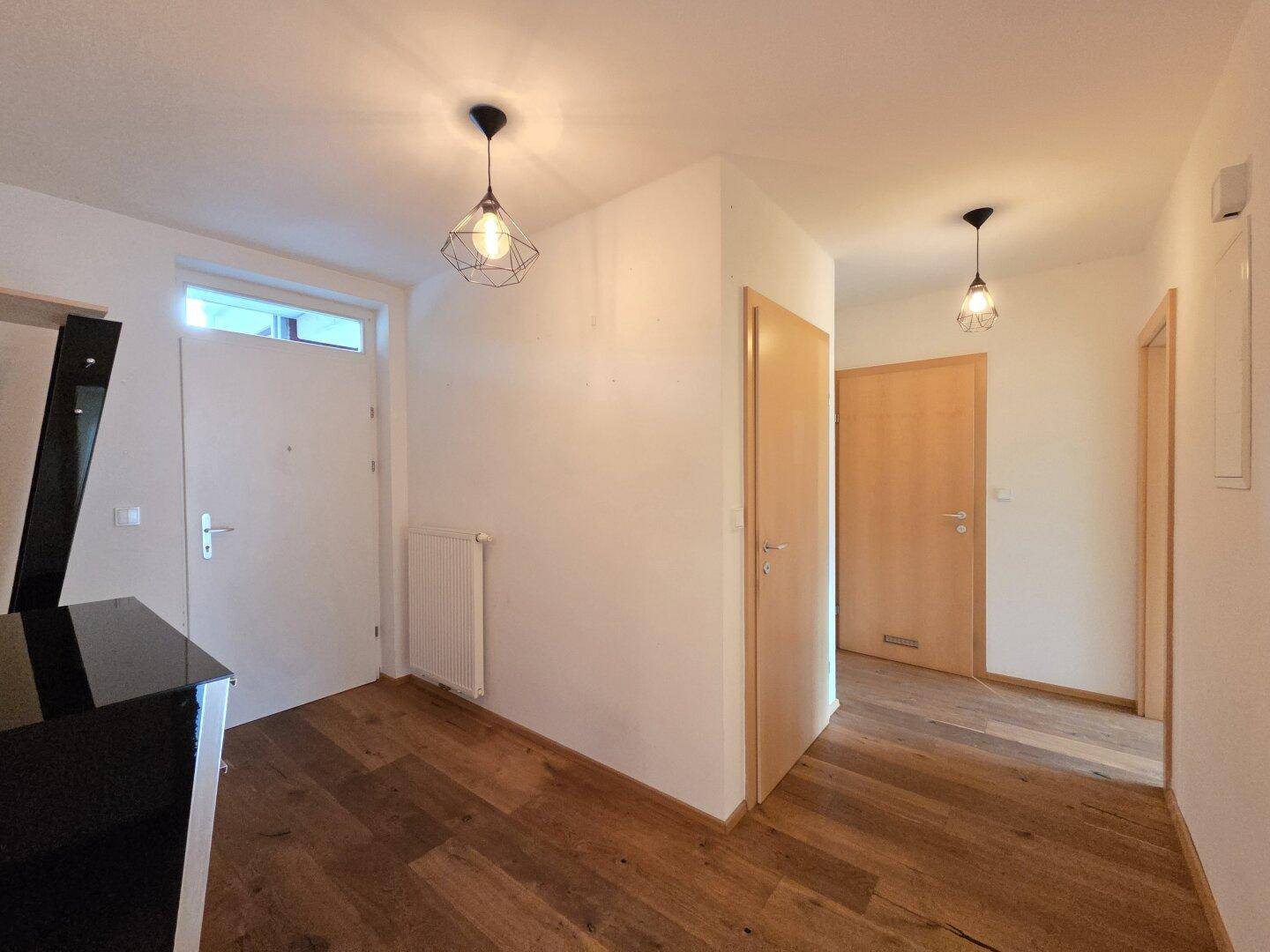 Eingangsbereich mit Holzboden, modernen Leuchten und Zugang zu verschiedenen Räumen.