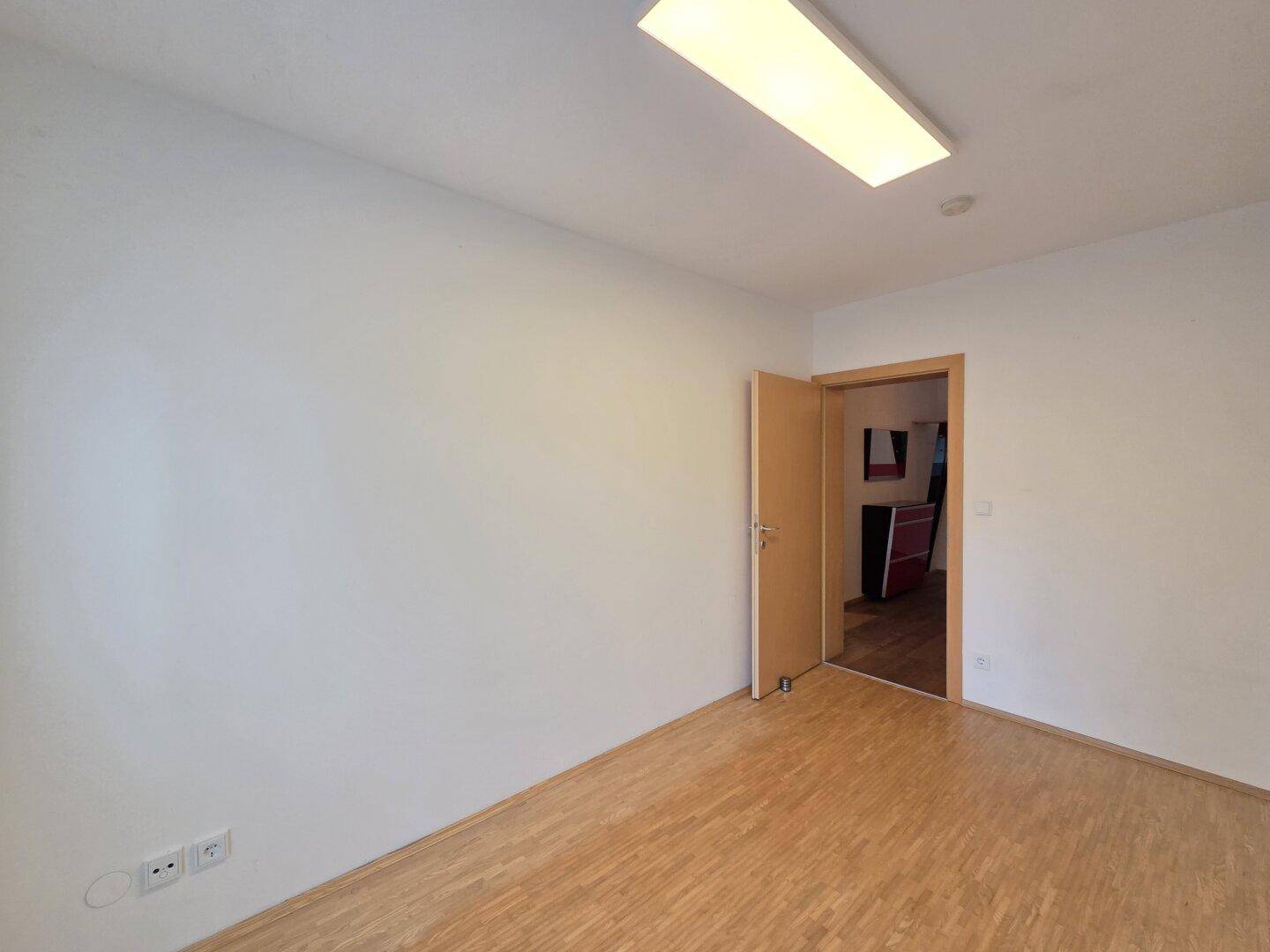 Helles Zimmer mit Laminatboden und Zugang zu einem weiteren Raum.