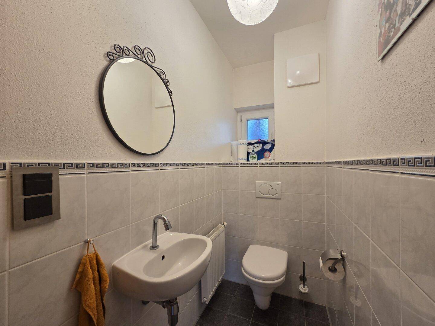 Gäste-WC mit kleinem Waschbecken, Toilette und Fenster.