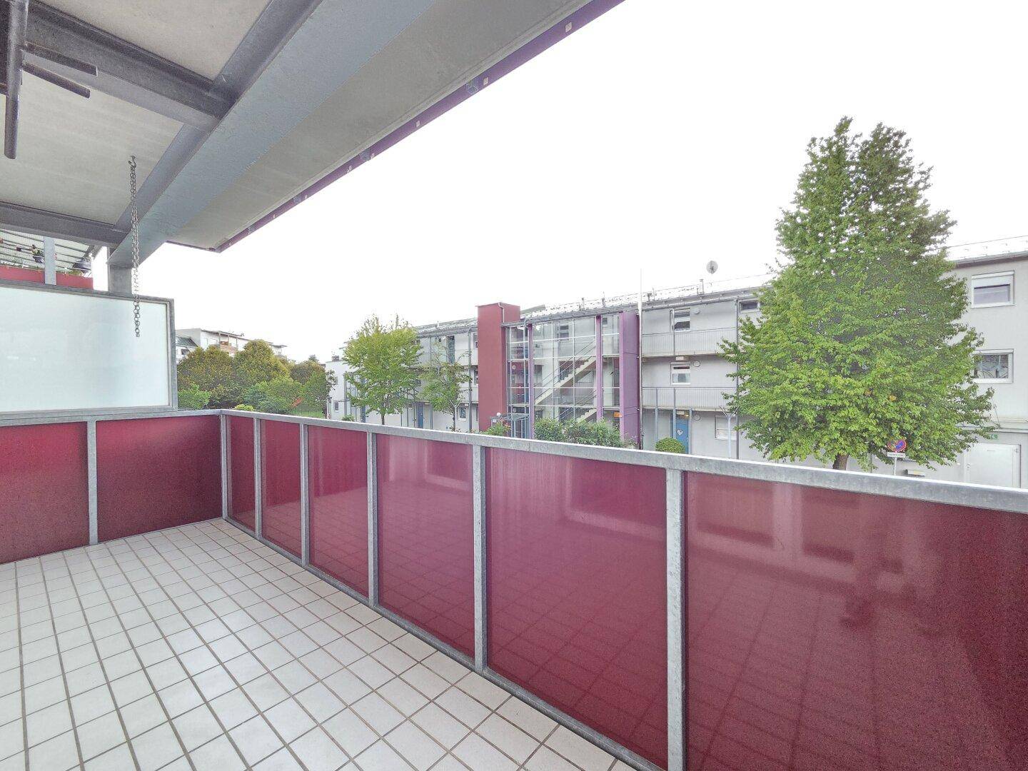 Geräumiger Balkon mit Fliesenboden und roter Brüstung, Blick auf die Umgebung.