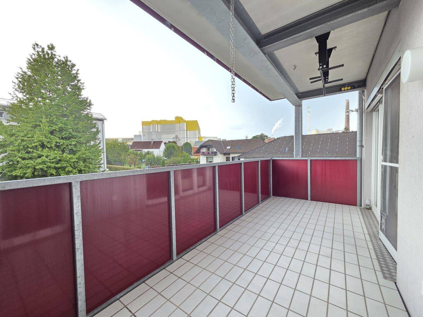 Großer Balkon mit Fliesenboden und roter Brüstung, bietet Platz für Sitzgelegenheiten.