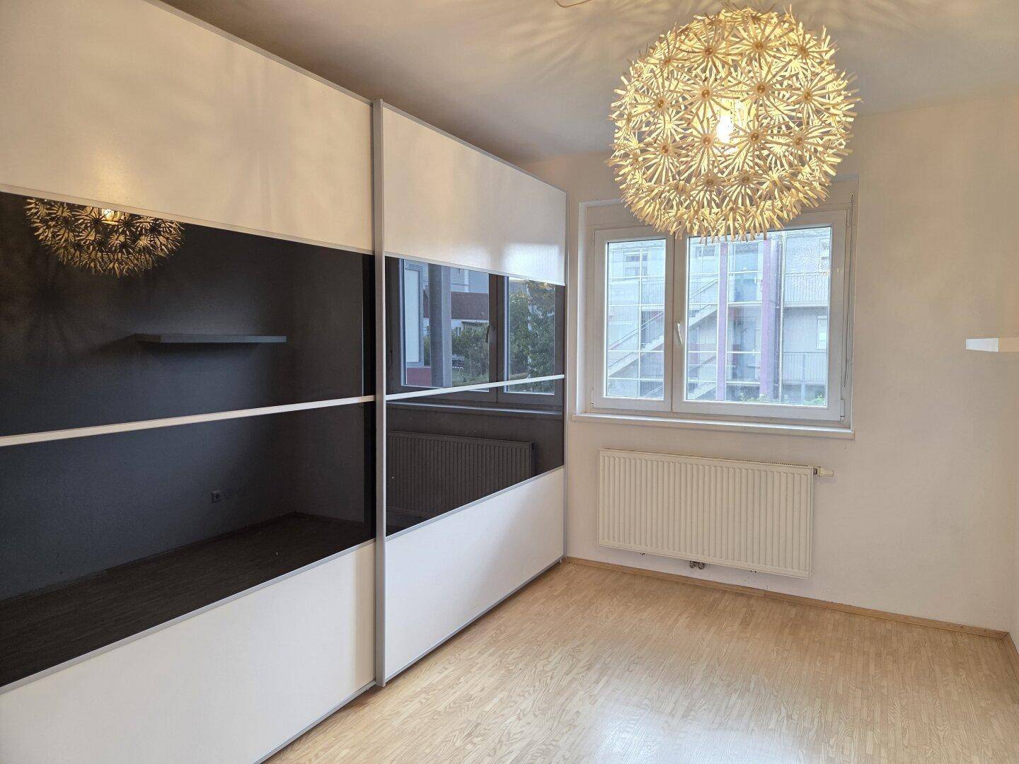 Schlafzimmer mit großem Einbauschrank, Laminatboden und Fenster mit Blick nach draußen.