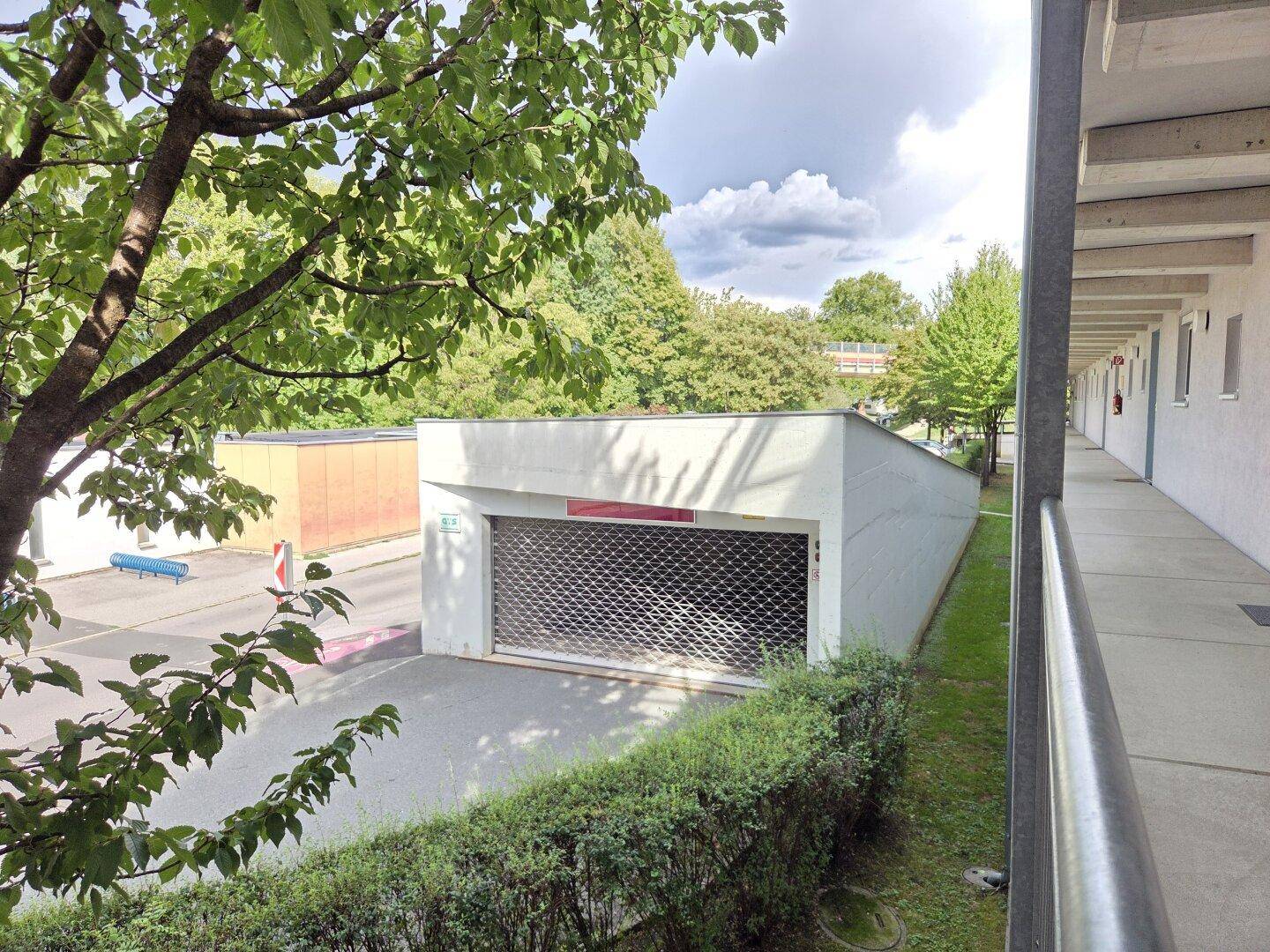 Außenansicht der Tiefgarageneinfahrt mit Rolltor und umgebender Grünfläche.