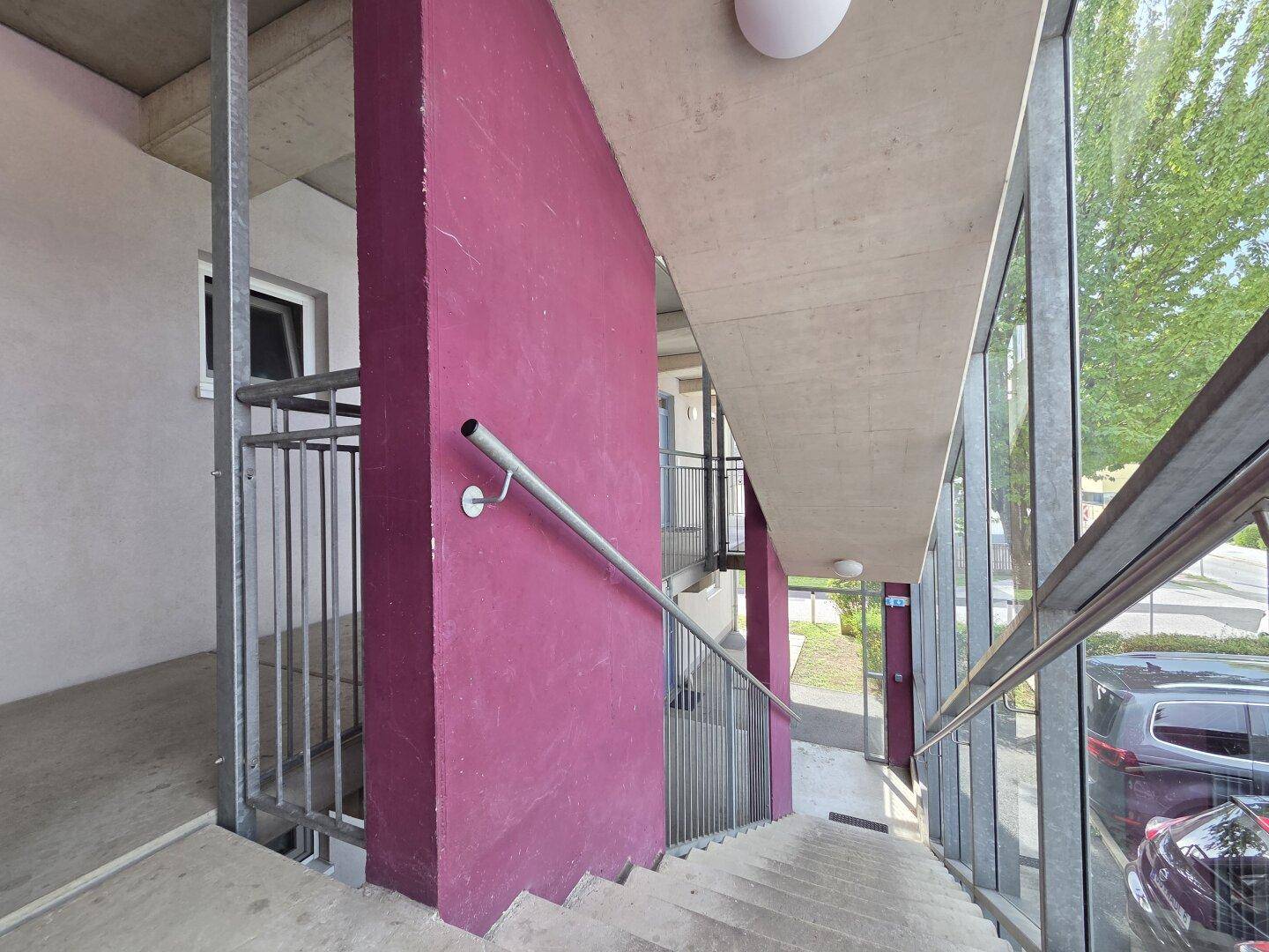 Treppenhaus mit Handlauf und großen Fenstern, bietet Zugang zu den Etagen.