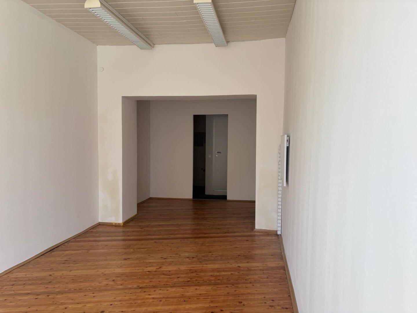 Geräumiger Innenraum mit Holzboden und offenem Durchgang zu einem weiteren Bereich.
