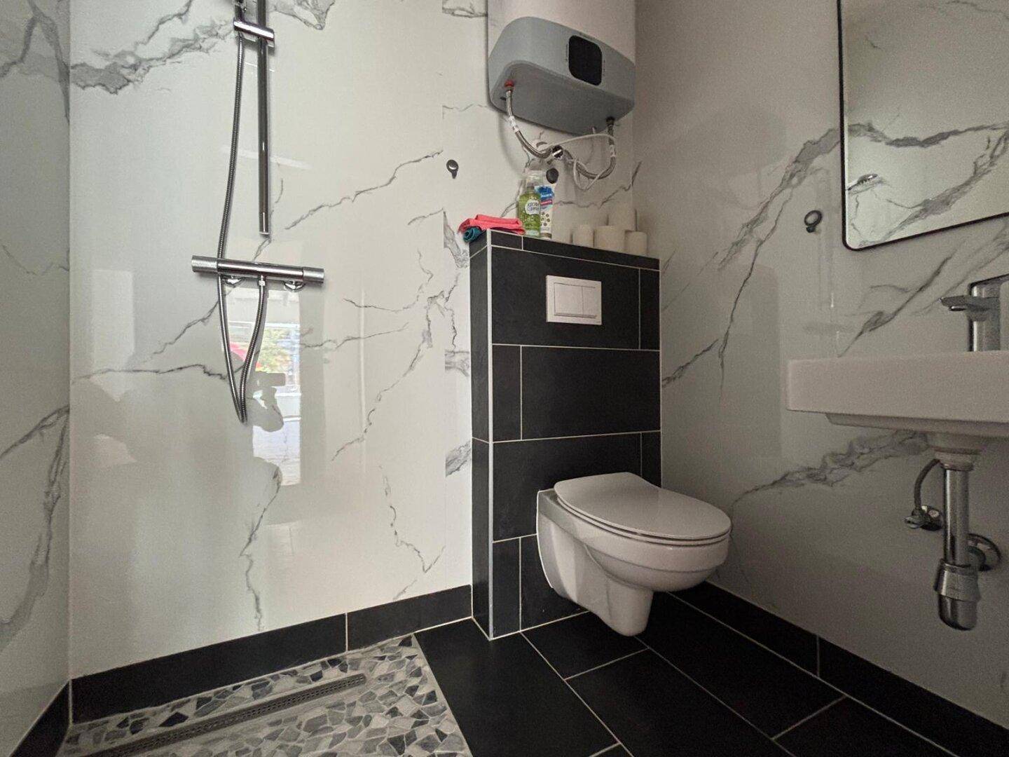 Modernes Badezimmer mit schwarz-weißen Marmorfliesen, Dusche und wandhängendem WC.