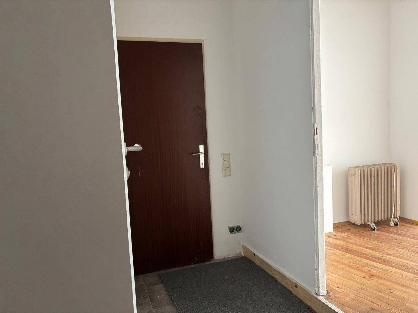 Eingangsbereich mit dunkler Holztür und Übergang zu einem Raum mit Holzboden.