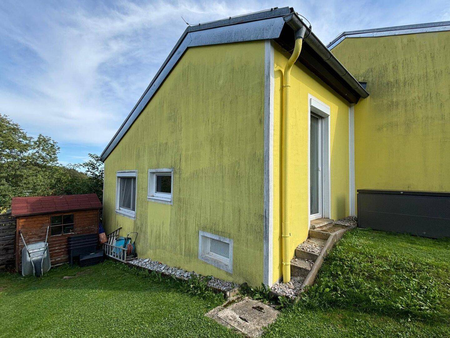 Seitenansicht des Hauses mit kleinem Gartenhaus und Zugang zum Gartenbereich.