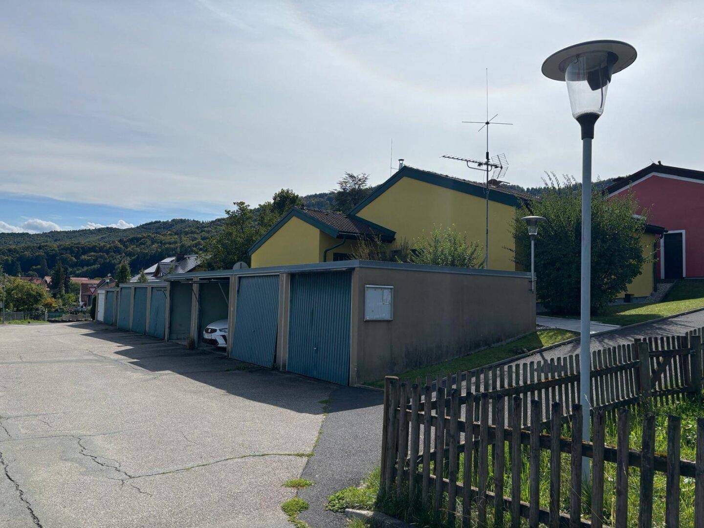 Reihe von Garagenstellplätzen mit dem Wohnhaus im Hintergrund und ländlicher Umgebung.
