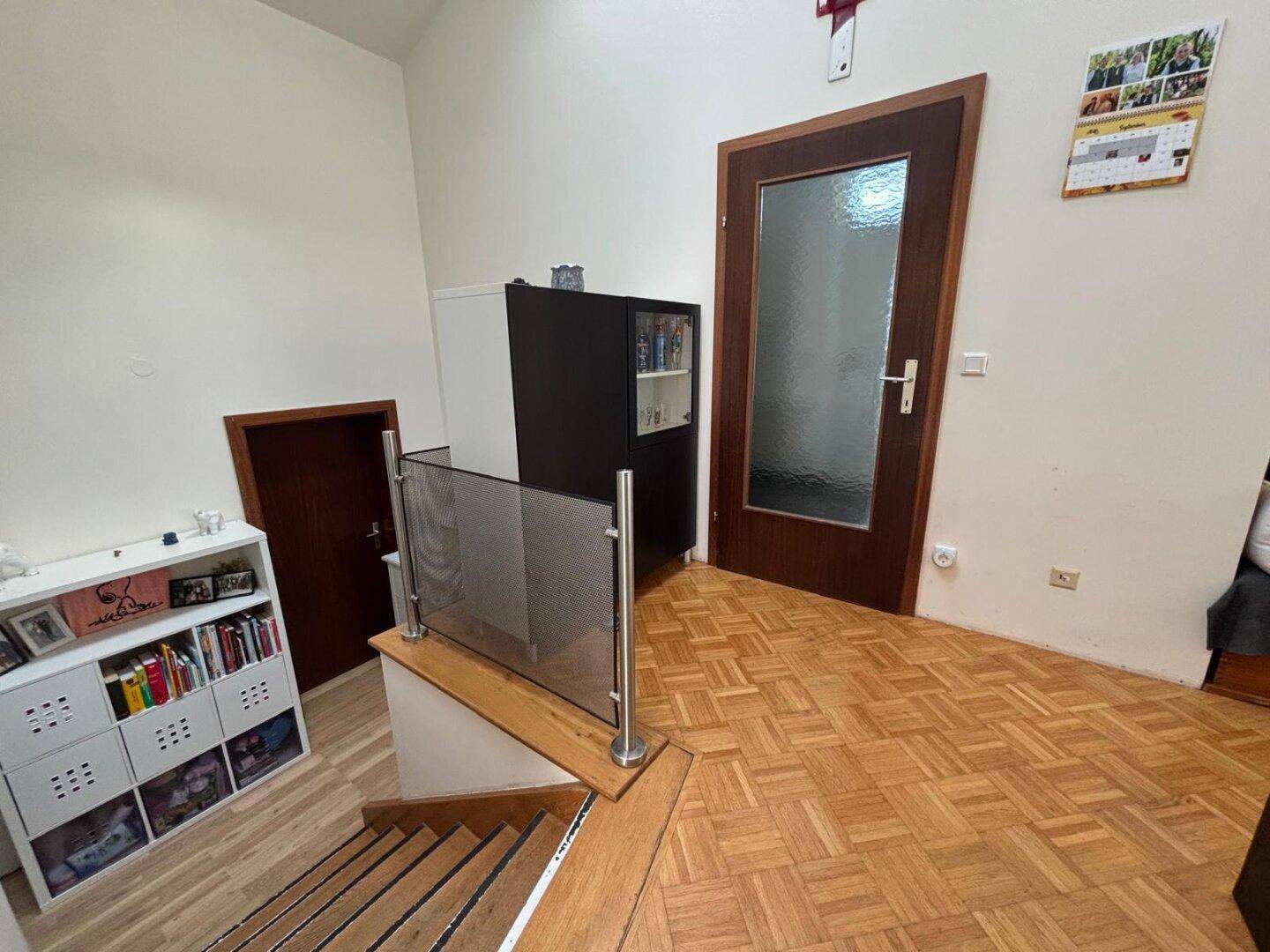 Treppenaufgang mit Holzstufen und Glasgeländer, führt zu einem hellen Flur.