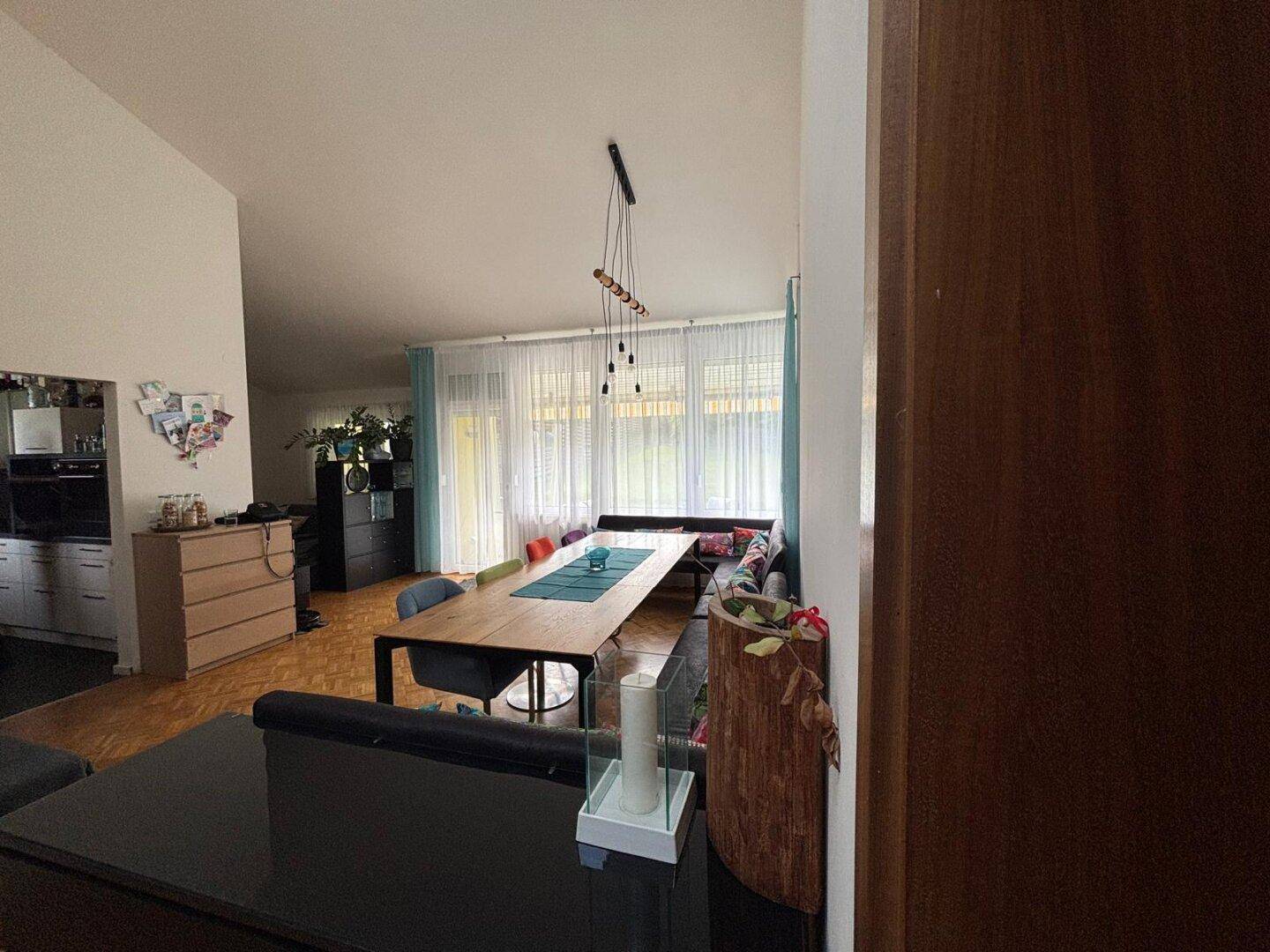 Heller Wohn-Essbereich mit großen Fenstern, Holzboden und moderner Einrichtung.
