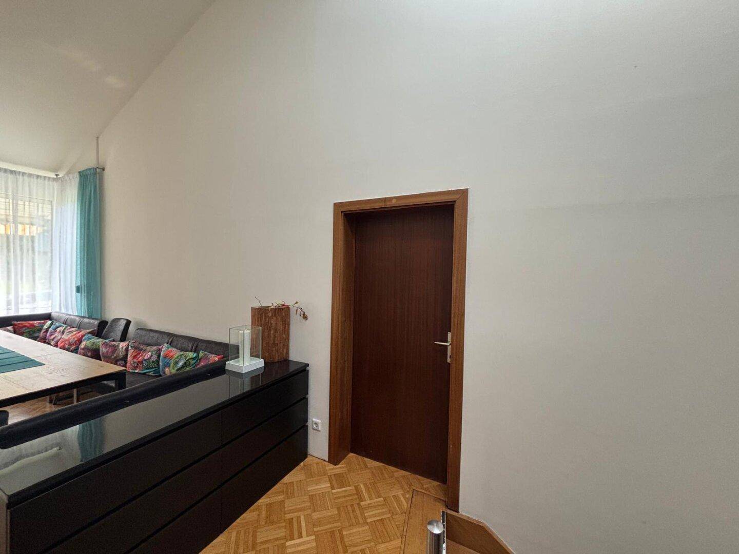 Teilansicht des Wohnbereichs mit Holzboden und Zugang zu einem weiteren Raum.